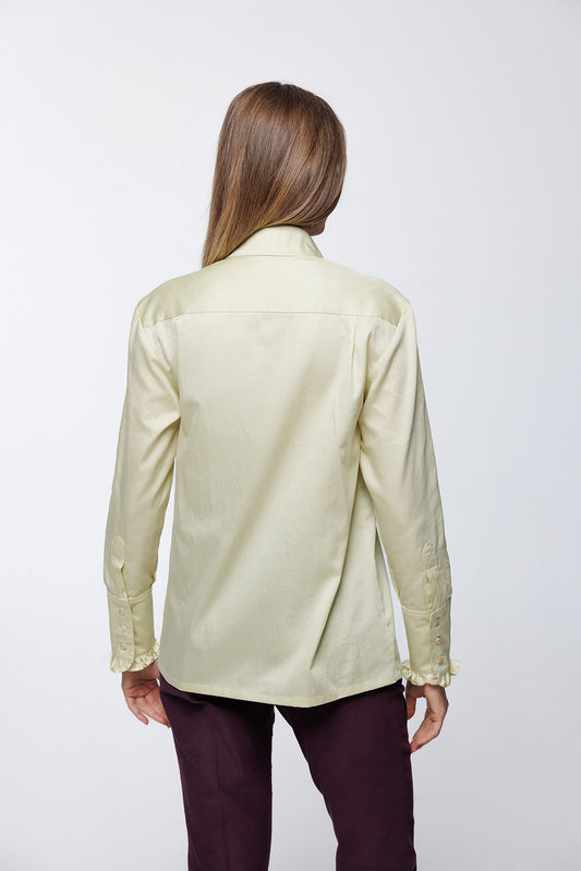 Gold‑green sateen cotton blouse with buttoned cuffs and smooth back panel, worn by a model with tailored trousers, back studio view.