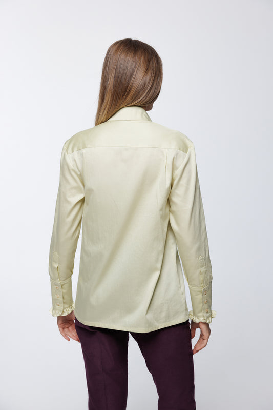 Gold‑green sateen cotton blouse with buttoned cuffs and smooth back panel, worn by a model with tailored trousers, back studio view.