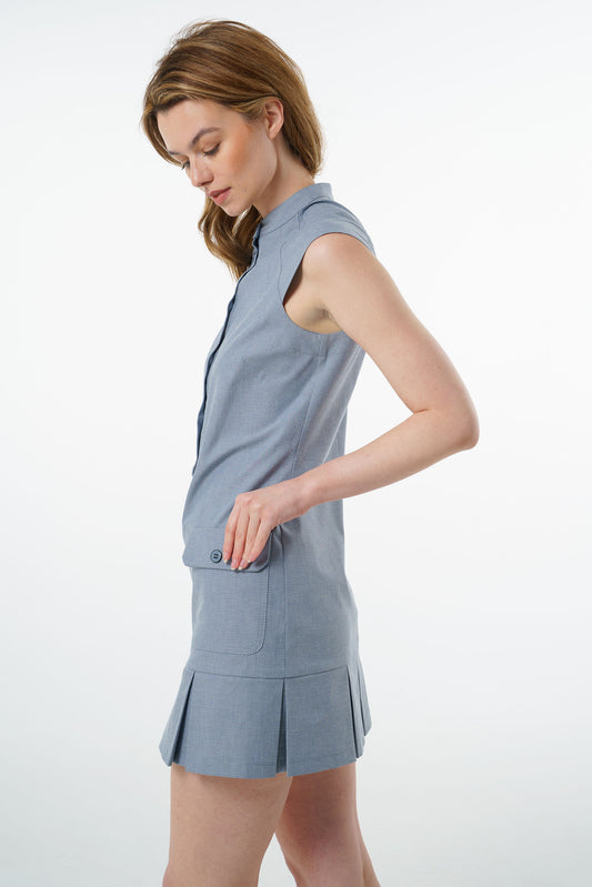Slate blue sleeveless cotton mini dress with flap pocket and pleated skirt, worn by a model, profile studio view.