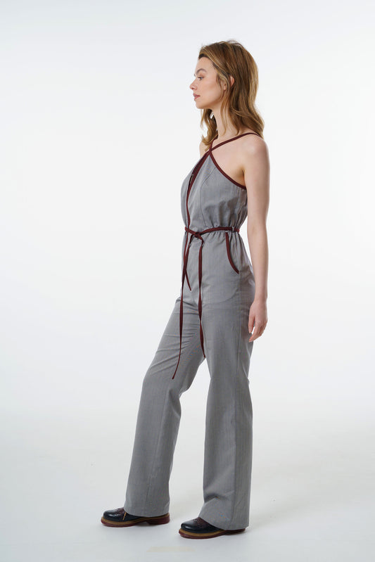 Grey straight‑leg jumpsuit with wine‑red trim, halter neckline, and tied belt, worn by a model, profile studio view.