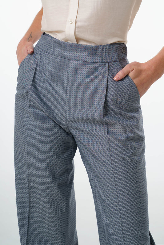 Mid‑waisted wide‑leg trousers in virgin wool featuring an adjustable side‑button waistband, front pleats, and tailored pocket construction, worn by a model, close‑up studio shot.