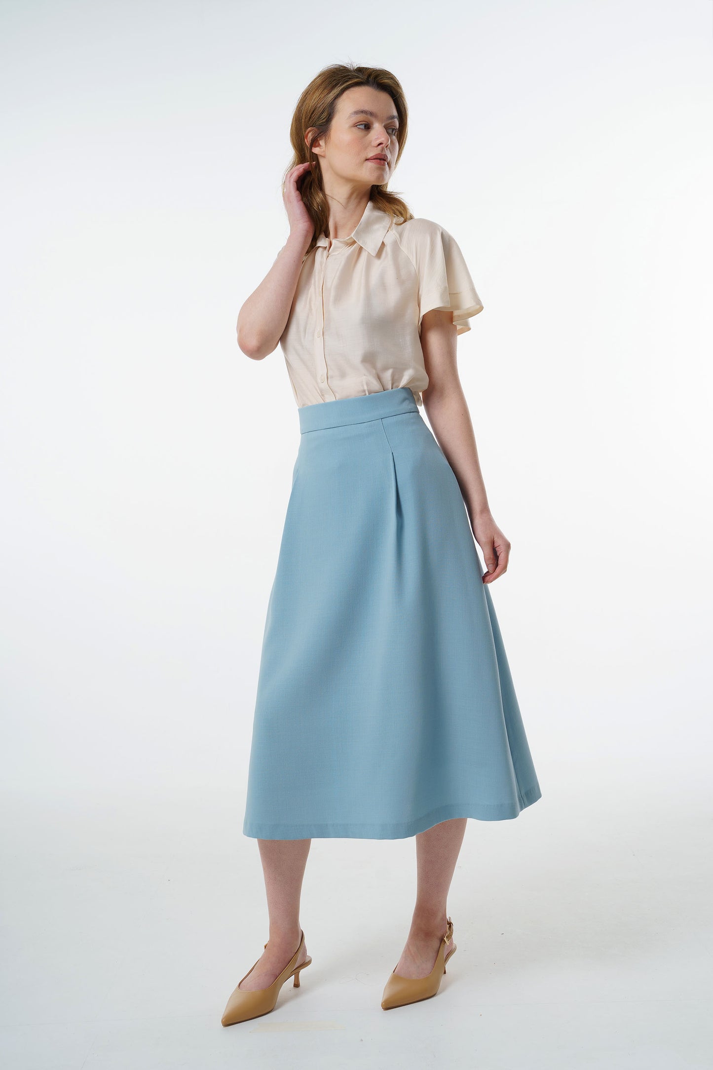 Light blue high‑waisted A‑line midi skirt in a virgin wool blend with front pleat detail, worn by a model, front studio view.