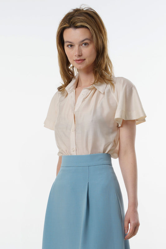 Ivory short‑sleeve silk–viscose blouse with flared raglan sleeves and button‑front neckline, worn by a model with a light blue A‑line skirt, front studio view.