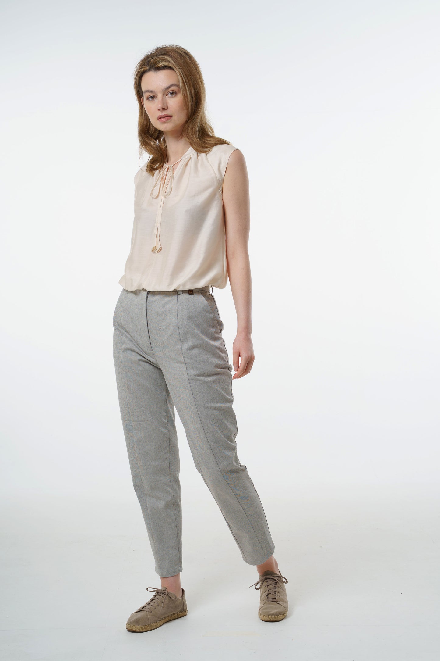 Light grey tapered carrot‑leg trousers in a cotton blend with high waist and tailored front seam, worn by a model, full‑length front studio view.