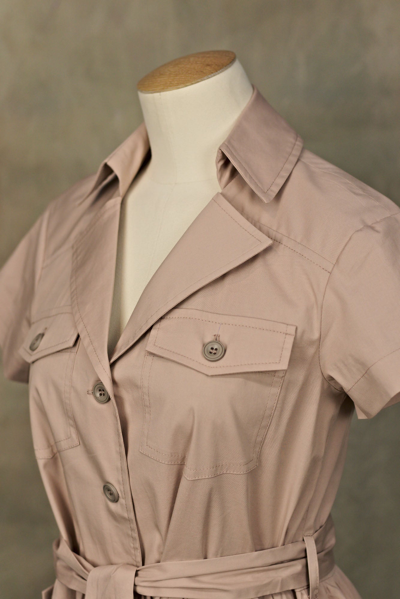 Close‑up of a dusty mauve cotton button‑down shirt-dress on a mannequin, showing collared neckline, chest and tied fabric belt.