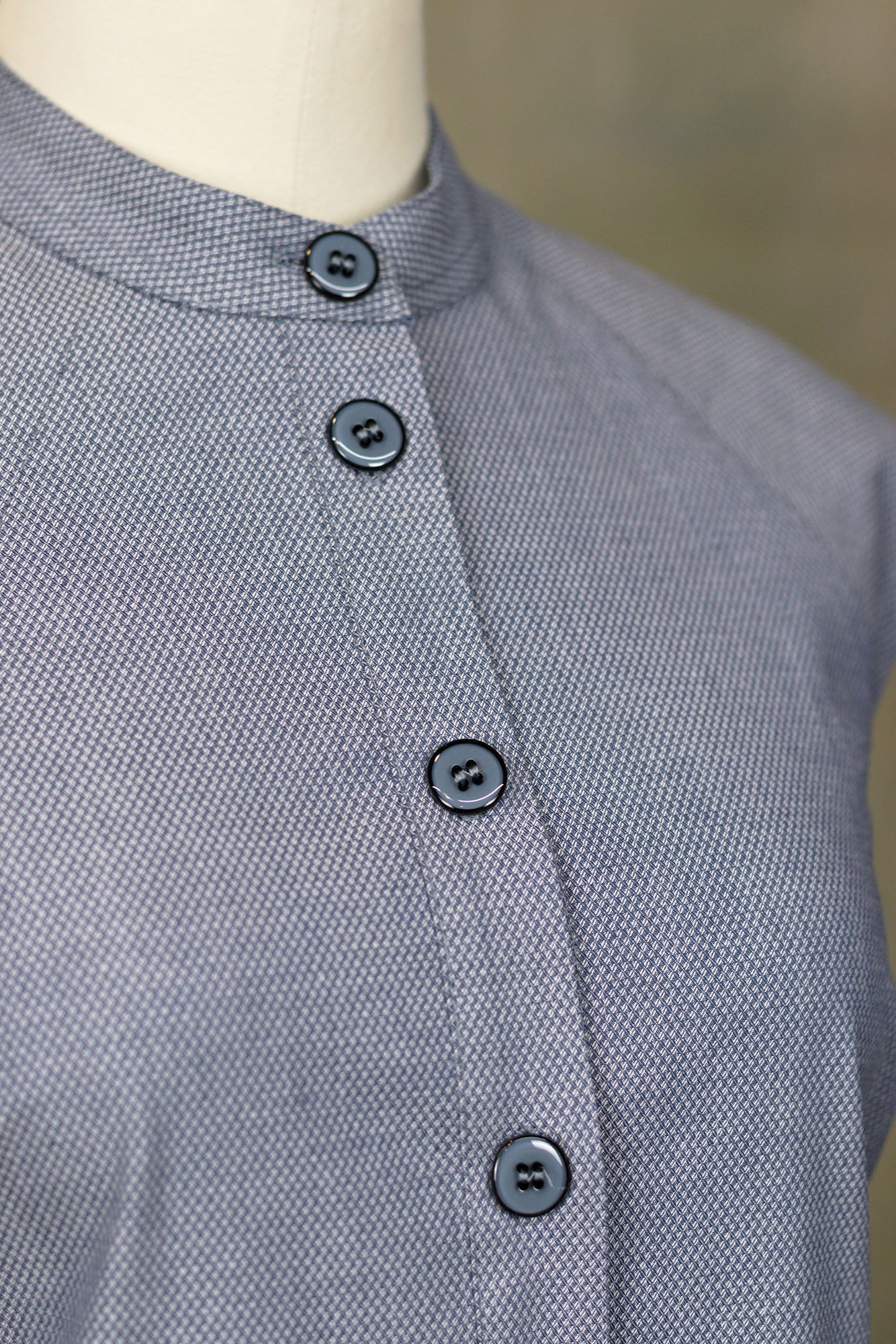 Slate blue sleeveless cotton mini dress with button‑up front, high collar, on a mannequin, macro studio view.
