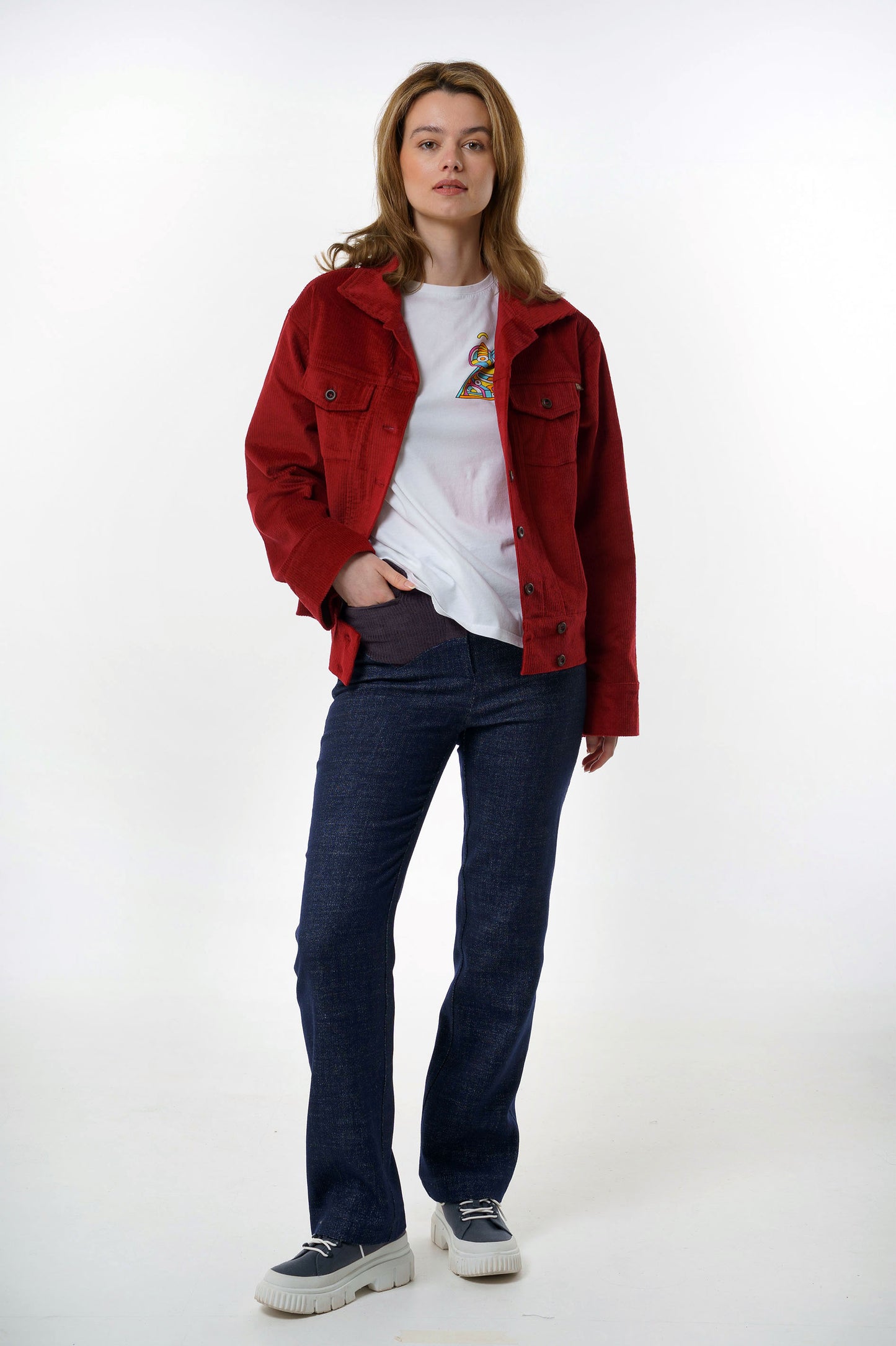 Full-body studio shot of a woman wearing a dark red corduroy jacket over a white t-shirt and dark blue contrast yoke trousers.  The trousers show a relaxed yet tailored straight-leg fit.