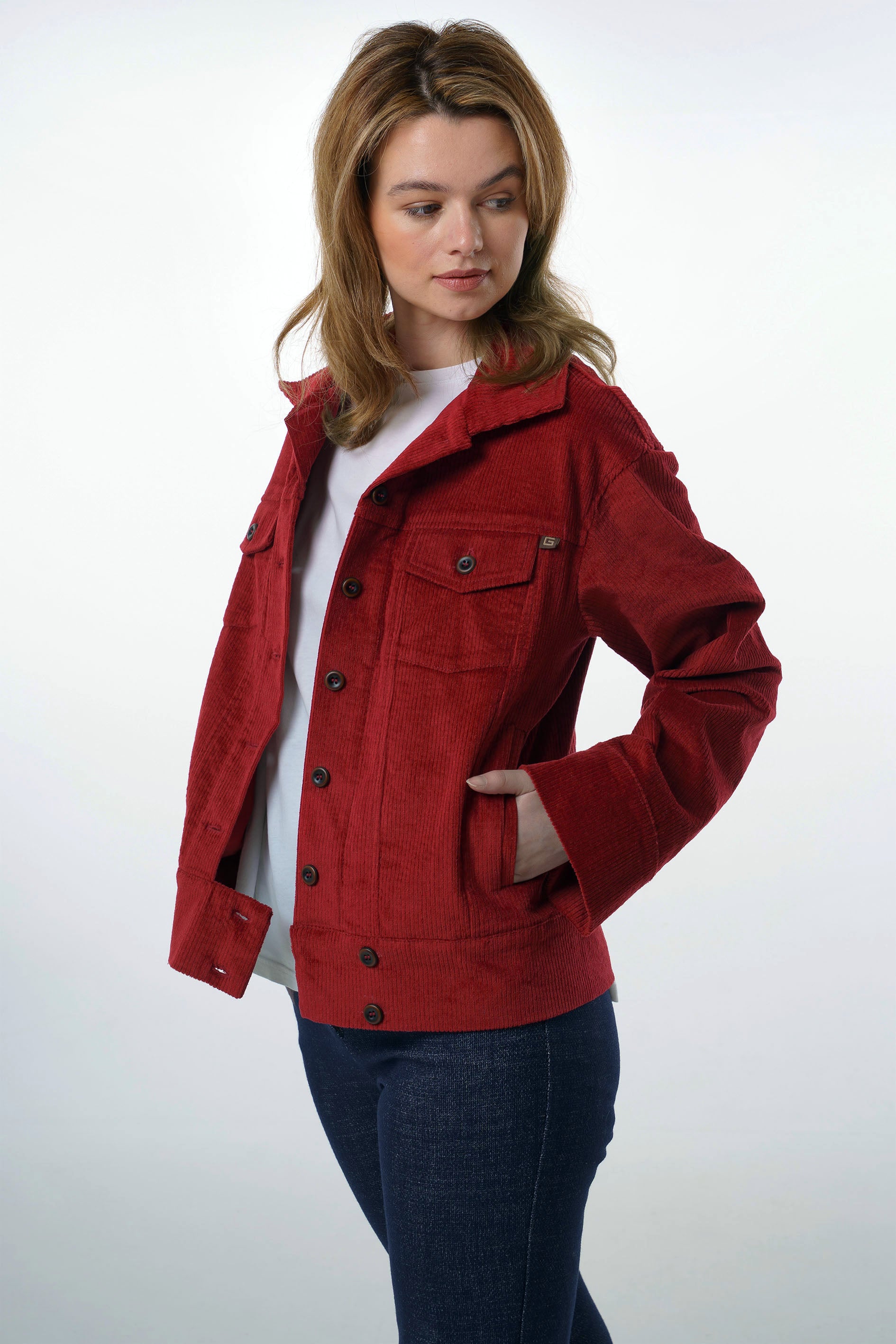 Side profile of a woman in a deep red corduroy jacket with a classic collar and button-down front, styled with dark denim.