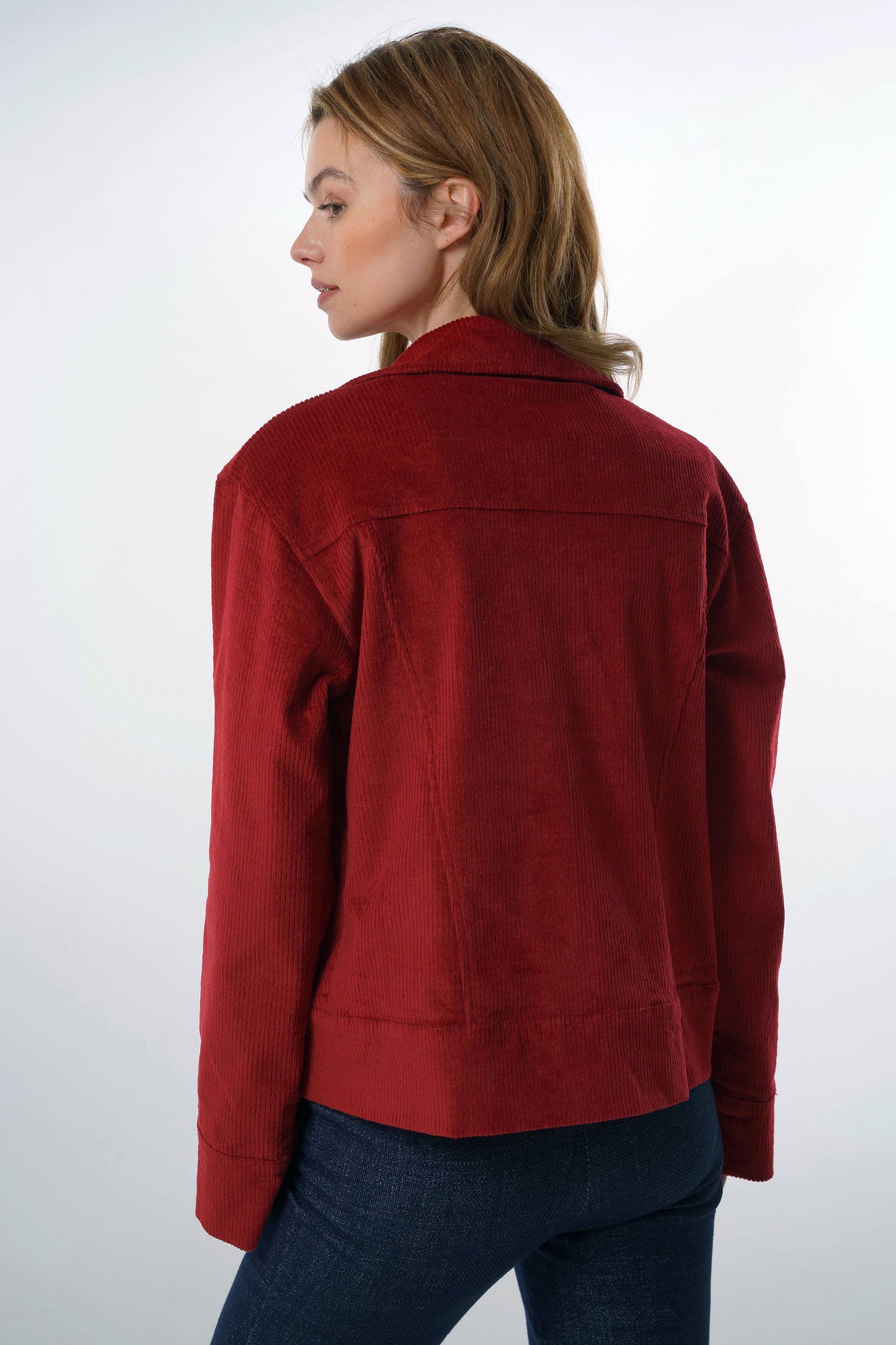 Back studio view of a dark red corduroy jacket on a model showing the clean yoke stitching and structured silhouette in a premium cotton blend.