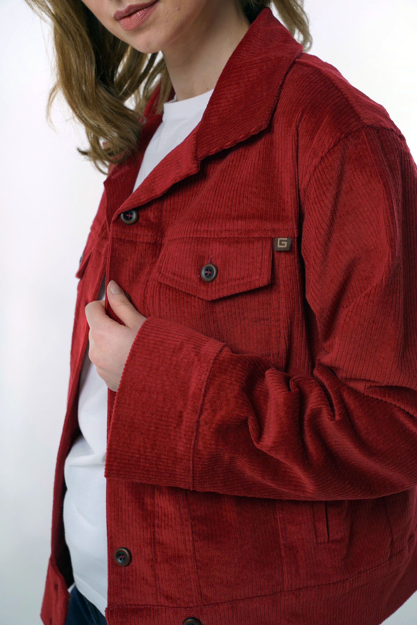 Detailed close-up of the chest pocket and button closure on a dark red corduroy jacket, emphasizing the high-quality fabric and craftsmanship.