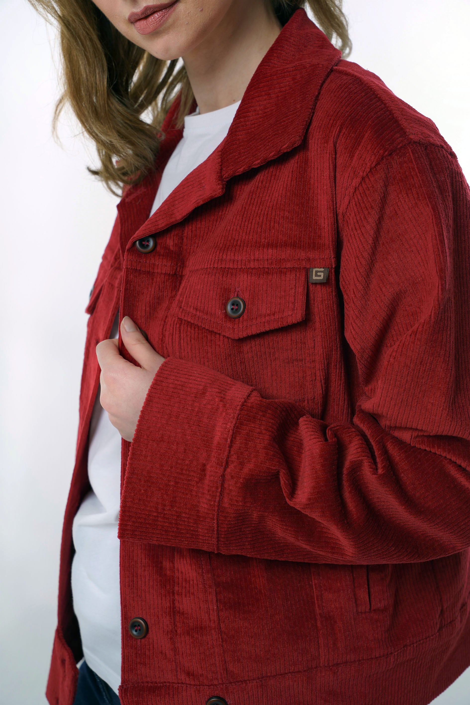 Detailed close-up of the chest pocket and button closure on a dark red corduroy jacket, emphasizing the high-quality fabric and craftsmanship.