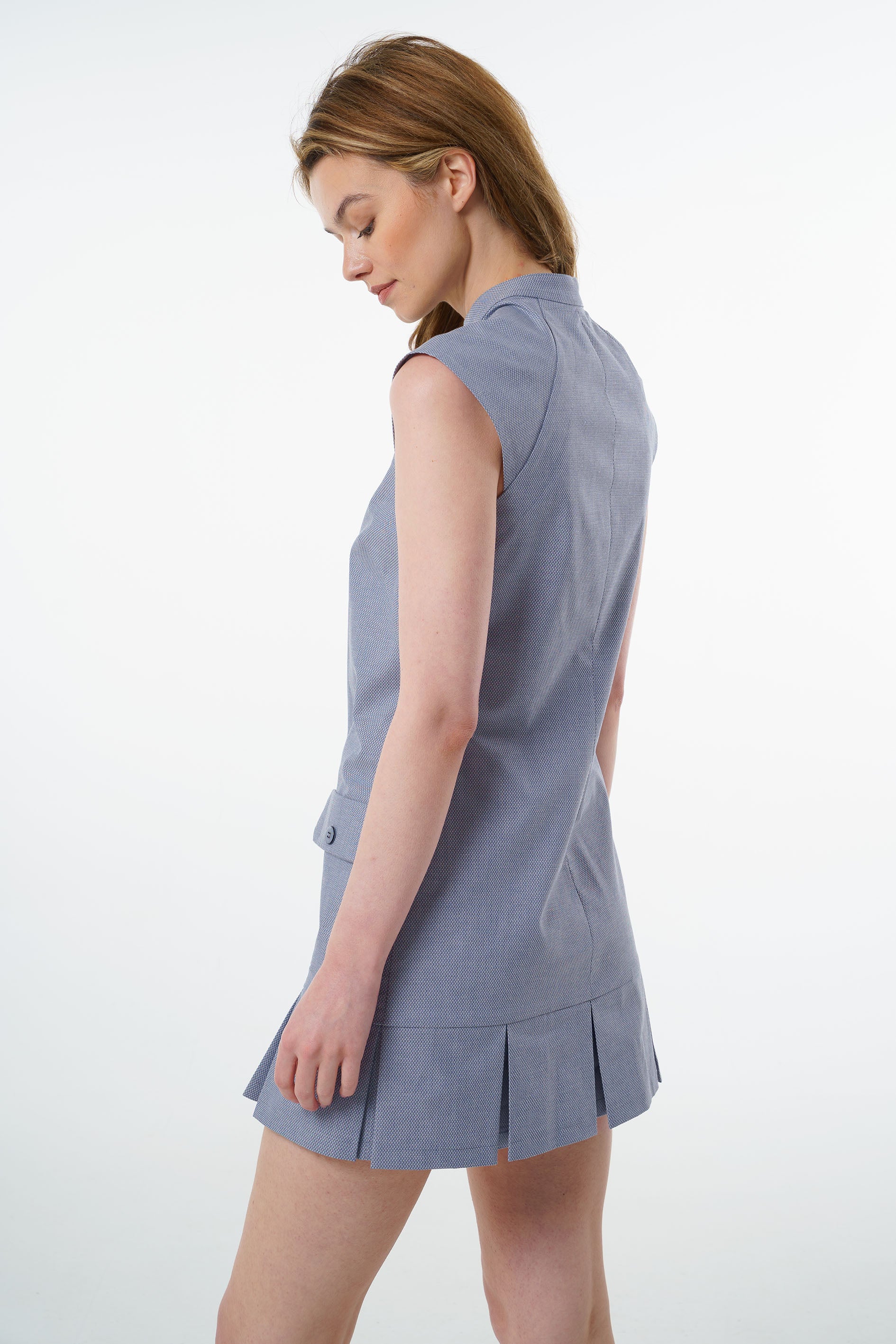 Slate blue sleeveless cotton dress with fitted bodice, textured fabric, and pleated mini skirt, worn by a model, angled studio view.