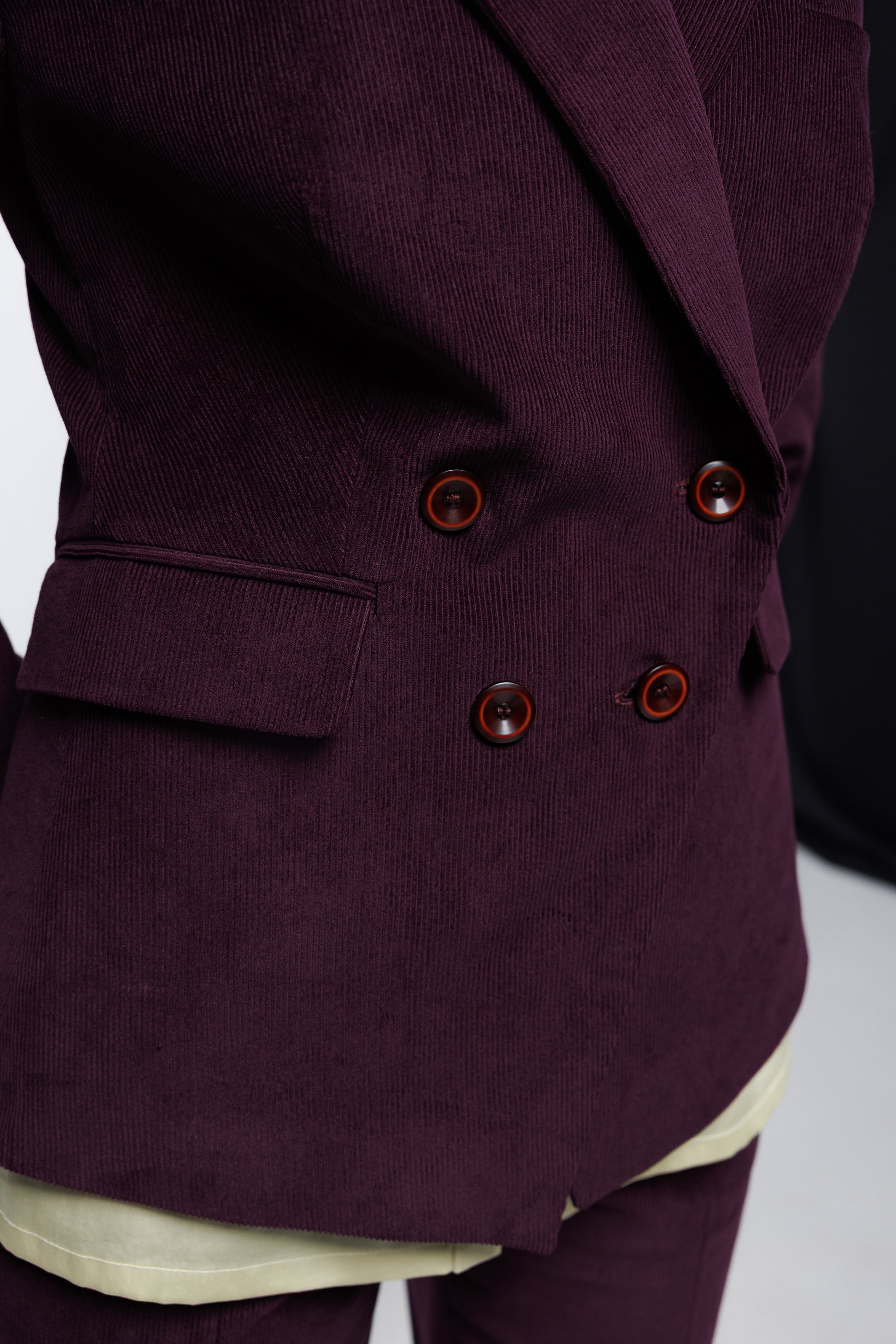 - Close‑up of deep‑purple corduroy double‑breasted blazer showing textured wale, flap pocket, and button detailing, worn by a model.