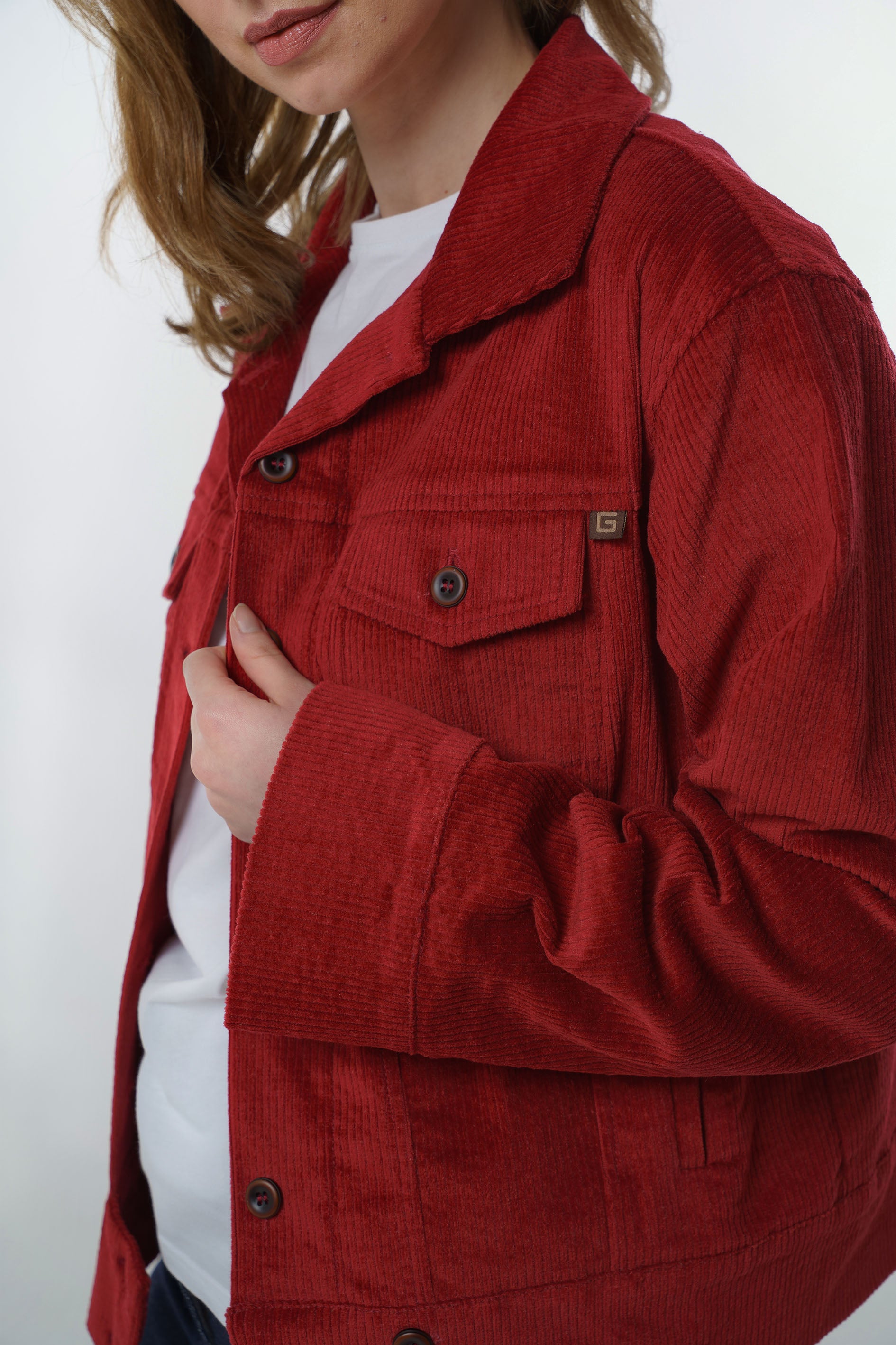 Detailed close-up of the chest pocket and button closure on a dark red corduroy jacket, emphasizing the high-quality fabric and craftsmanship.