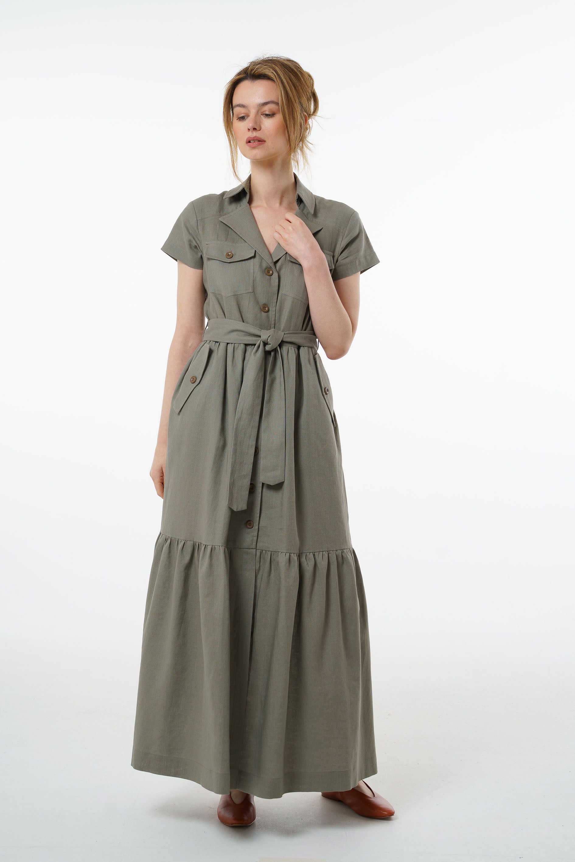 Olive green linen button‑down maxi dress with short sleeves, belted waist, chest pockets, and tiered skirt, worn by a model, front studio view.