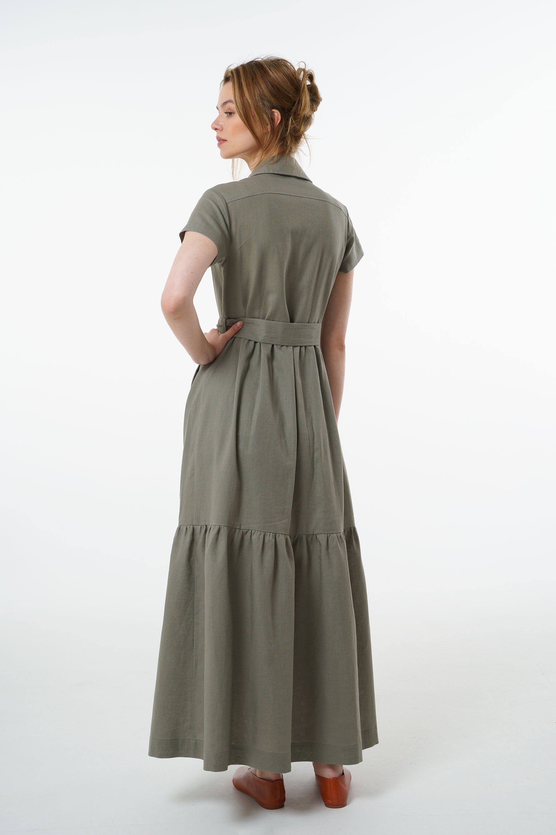 Back view of olive green linen button‑down maxi dress with belted waist and gathered tiered skirt, worn by a model.skirt. 