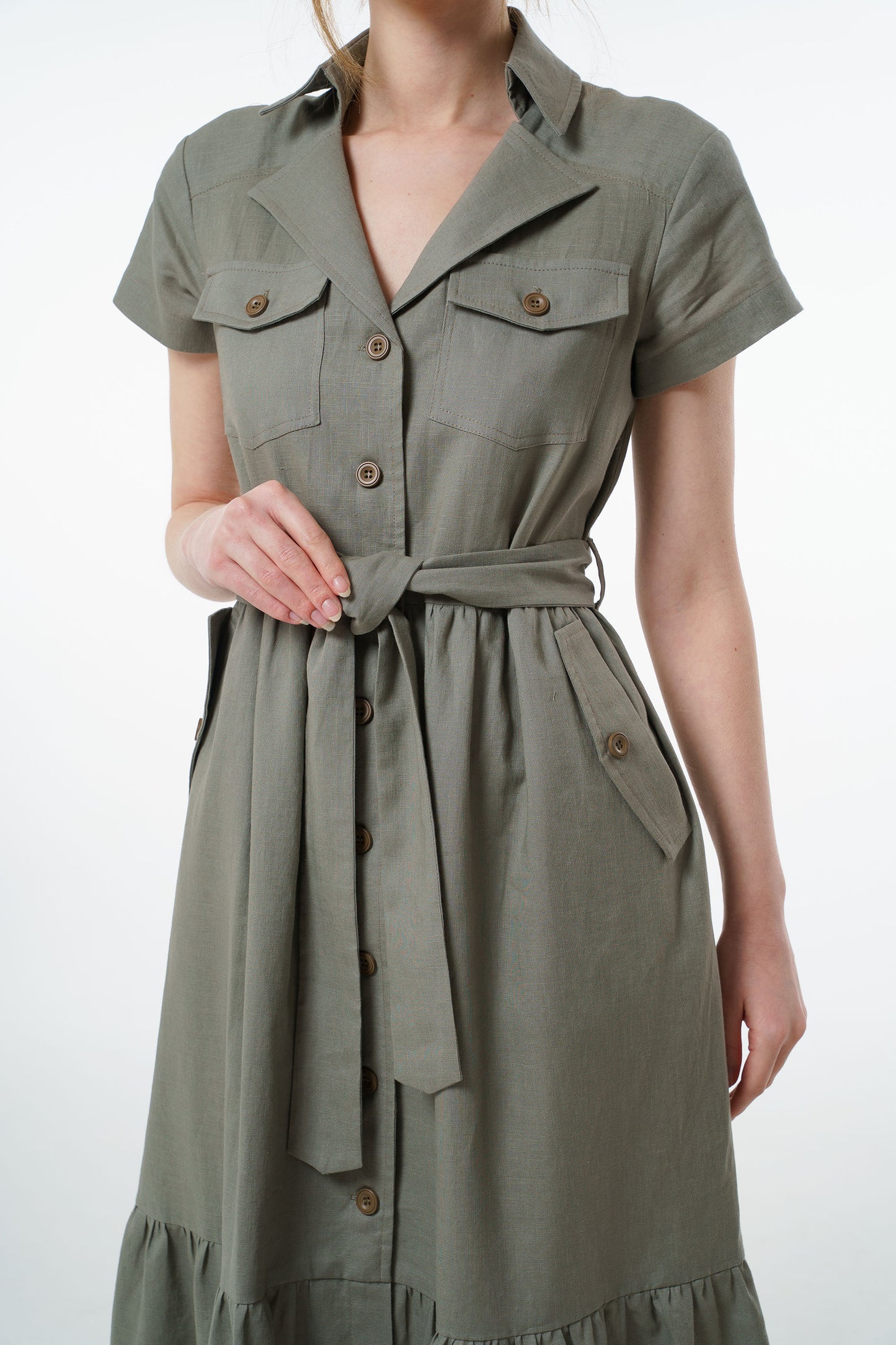 Olive green linen button‑down dress with collared neckline, chest pockets, and belted waist, worn by a model, front studio shot.