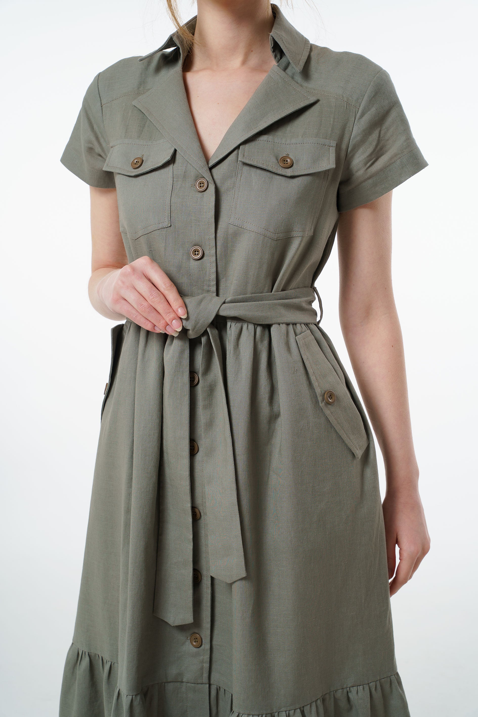 Olive green linen button‑down dress with collared neckline, chest pockets, and belted waist, worn by a model, front studio shot.