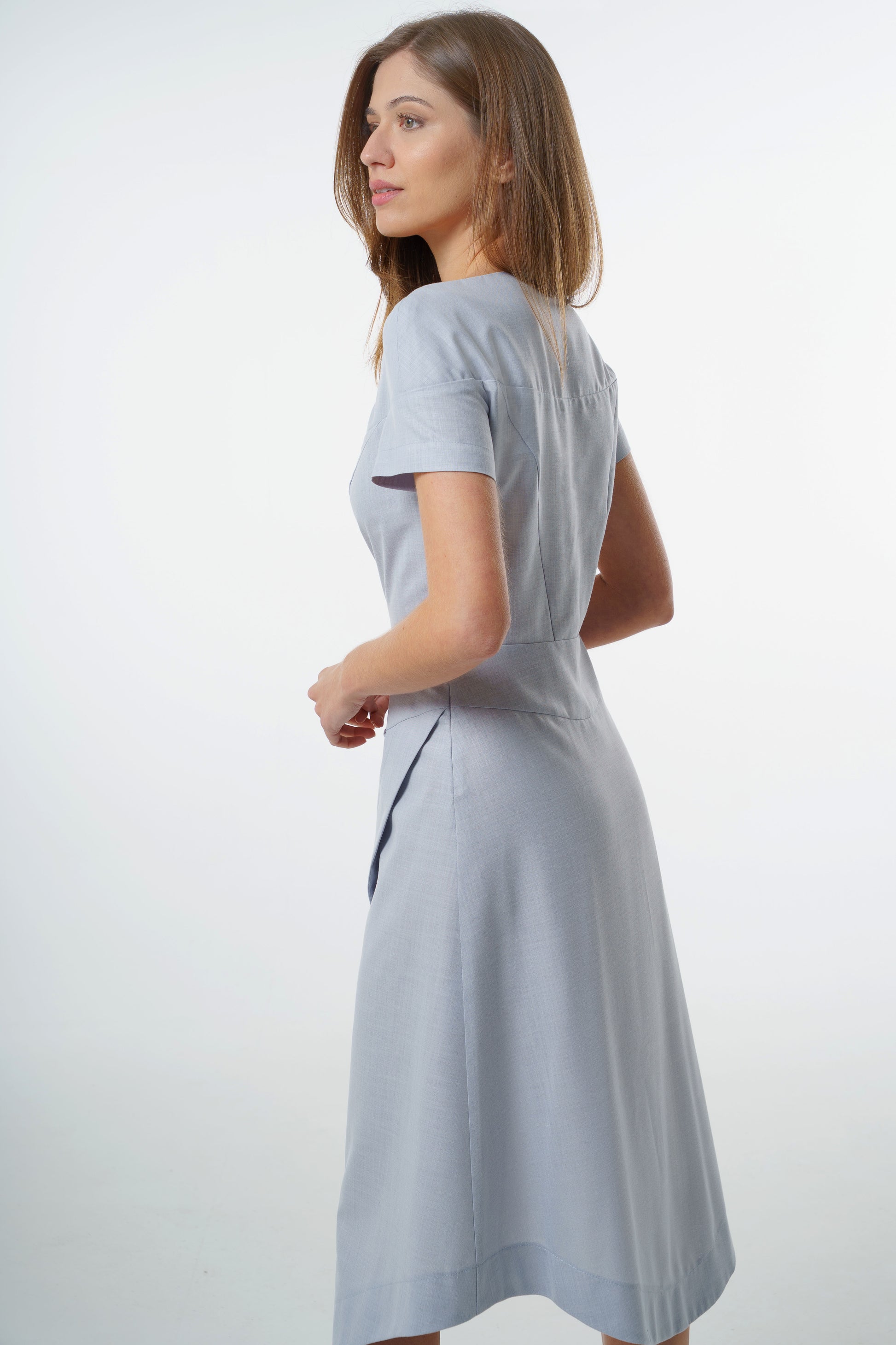 Pale blue tailored midi dress with fitted bodice and wrapped skirt, worn by a model, side‑back studio view.