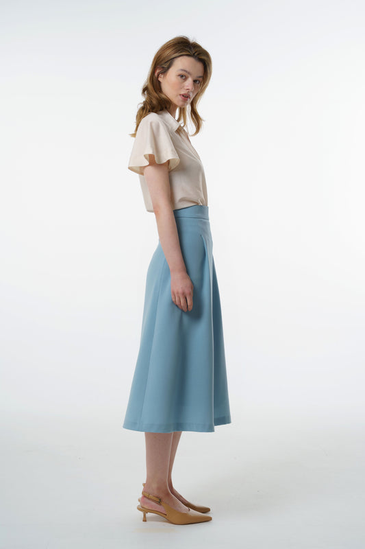 Light blue virgin‑wool A‑line midi skirt with high‑waisted fit and soft flare, worn by a model, profile studio view.