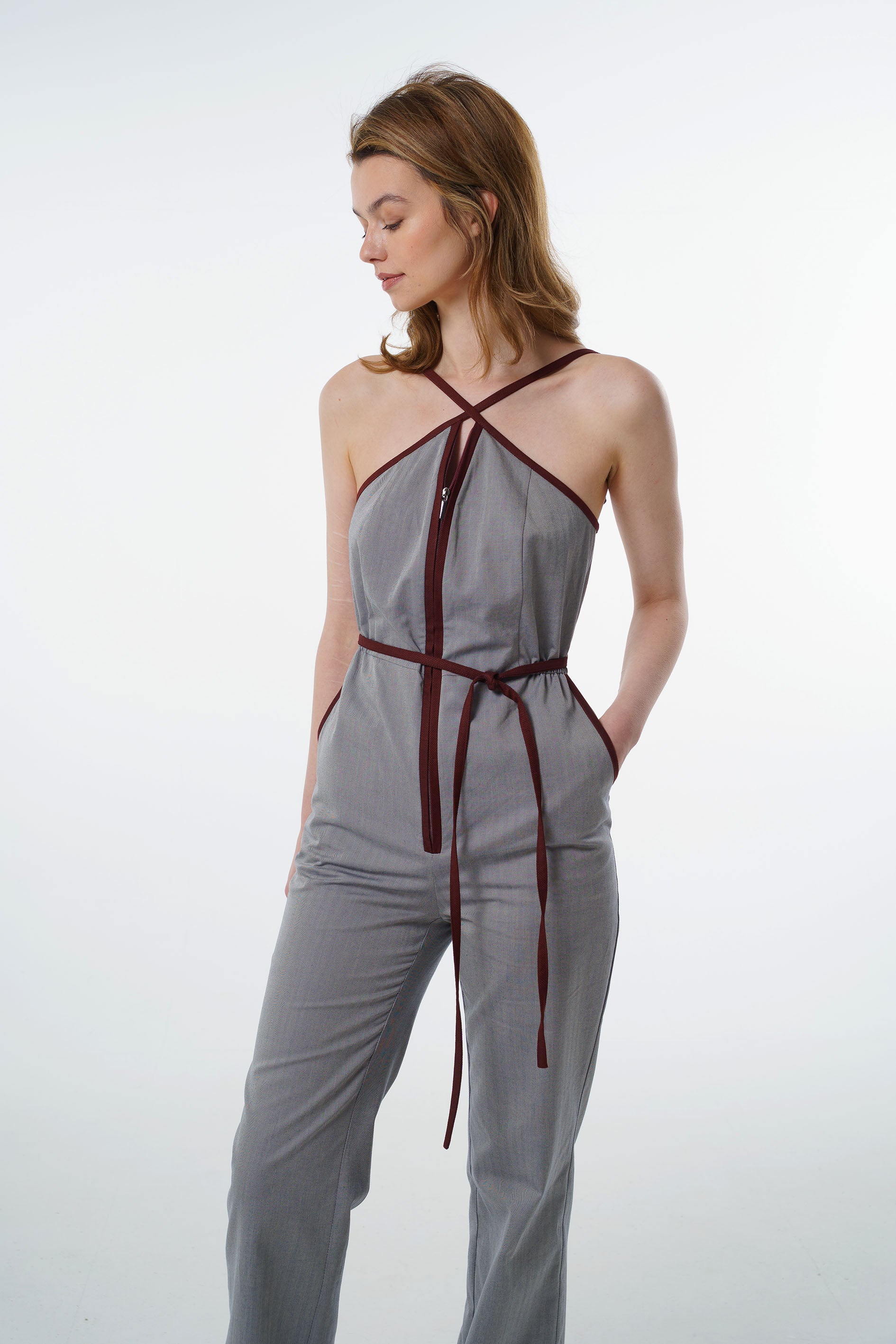 Grey jumpsuit with wine‑red trim, zip‑front closure, and side pockets, worn by a model, front studio view.