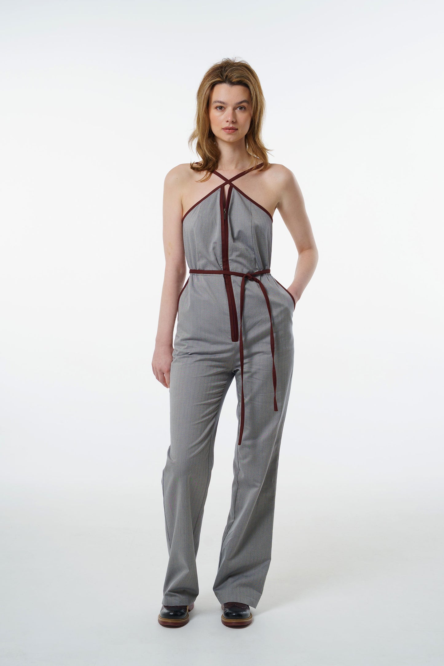 Grey straight‑leg jumpsuit with wine‑red trim, halter neckline, and zip‑front closure, worn by a model, front studio shot.