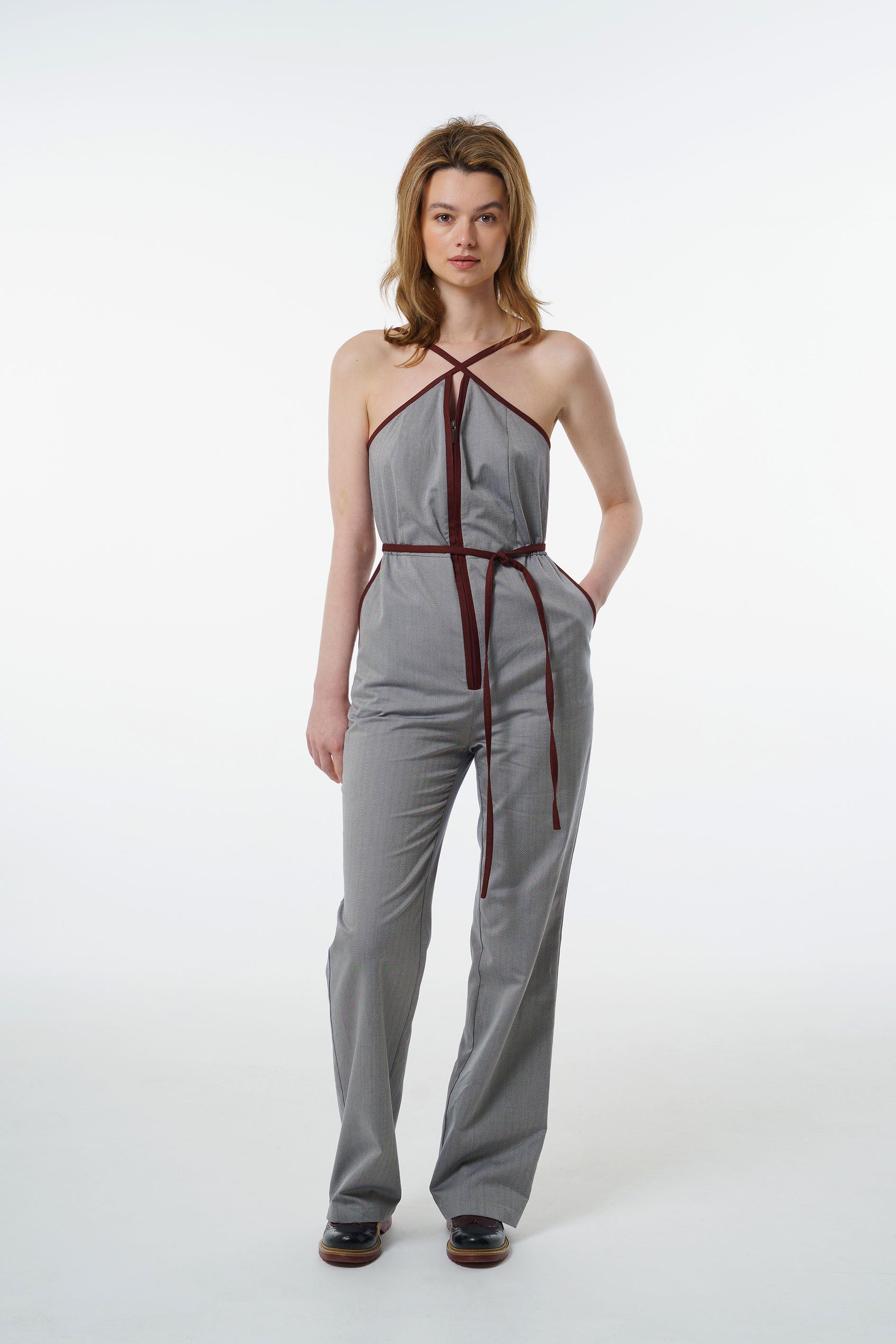 Grey straight‑leg jumpsuit with wine‑red trim, halter neckline, and zip‑front closure, worn by a model, front studio shot.