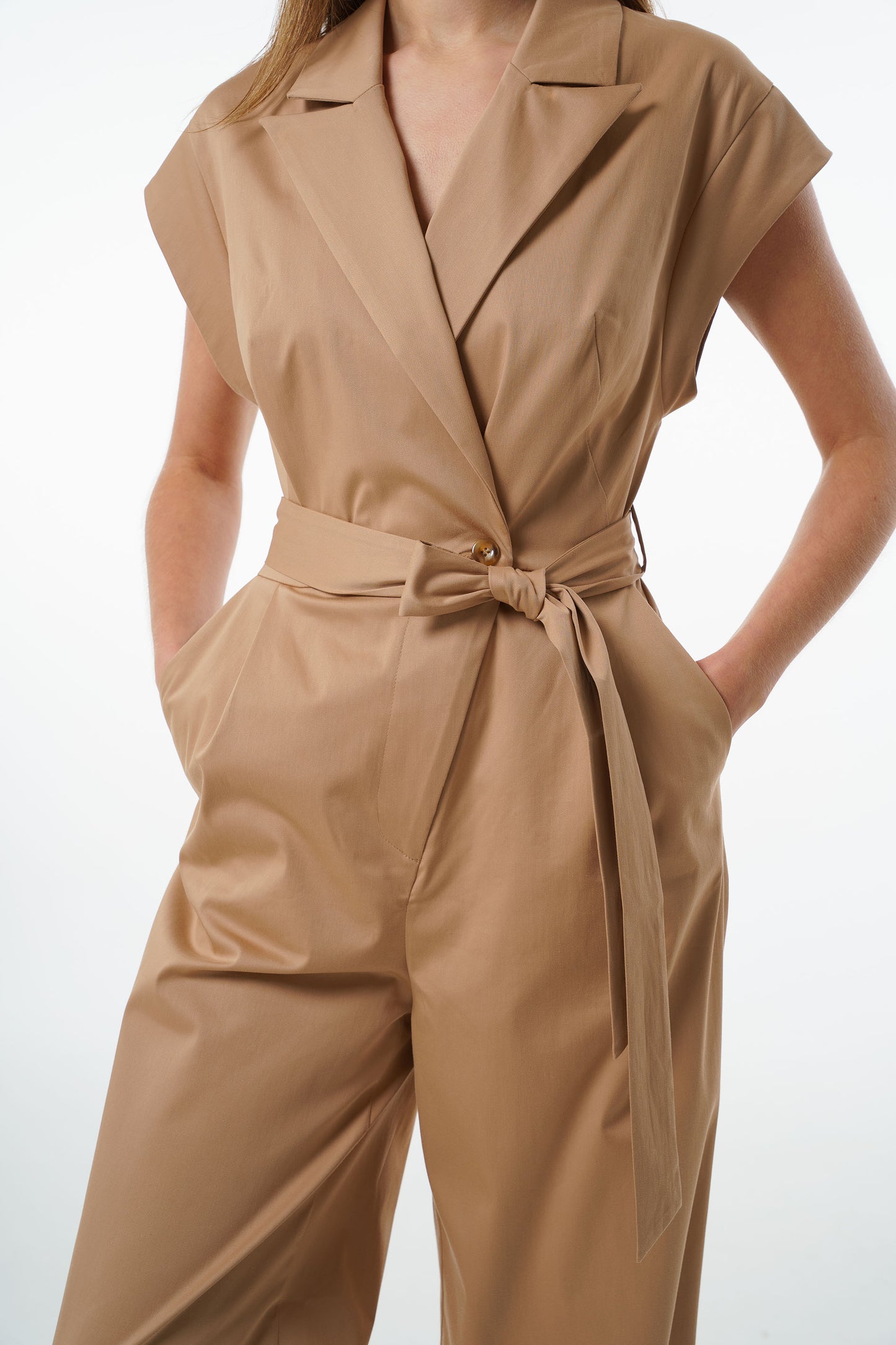 Close‑up of camel cotton–viscose wrap‑front jumpsuit showing notched collar, short sleeves, and tied waist, worn by a model.