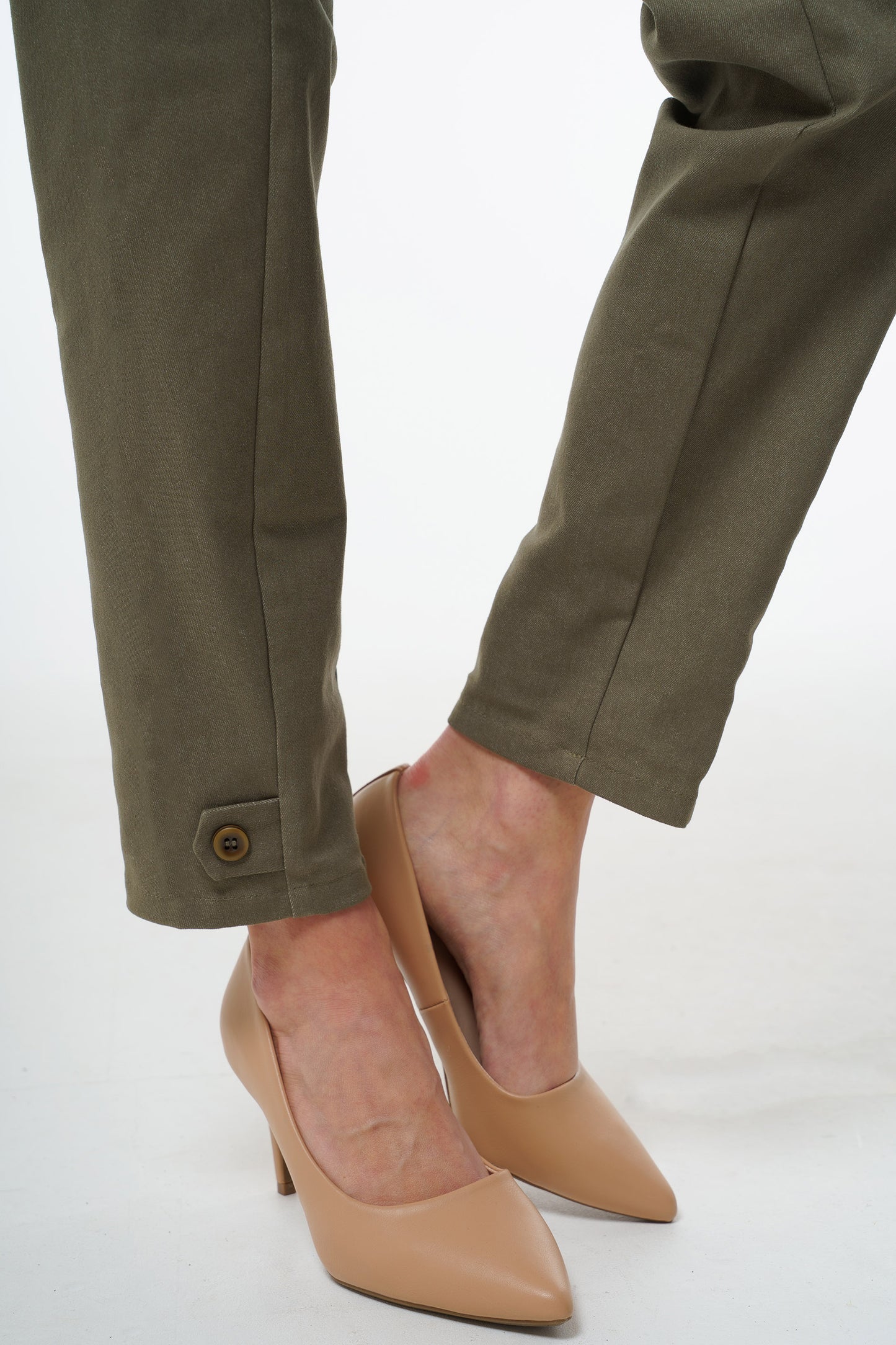 Close‑up of olive stretch denim trousers showing button‑accented ankle cuff and tailored hem, worn by a model.