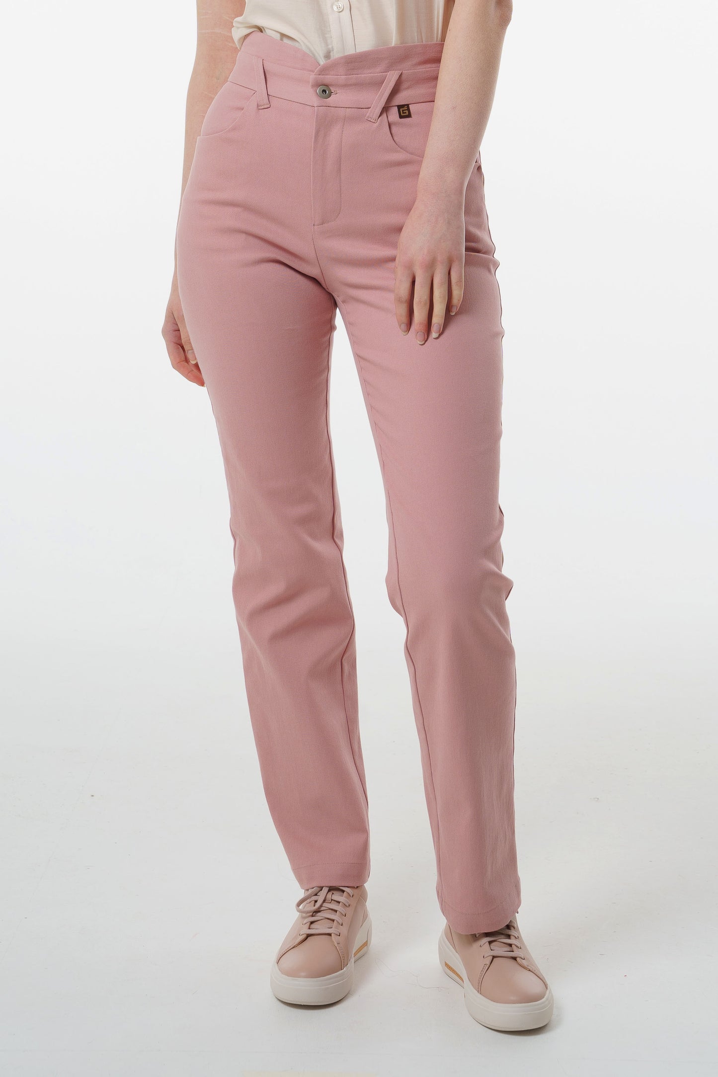 Close‑up of rose‑dust stretch denim trousers showing straight‑leg hem and pastel sneakers, worn by a model.
