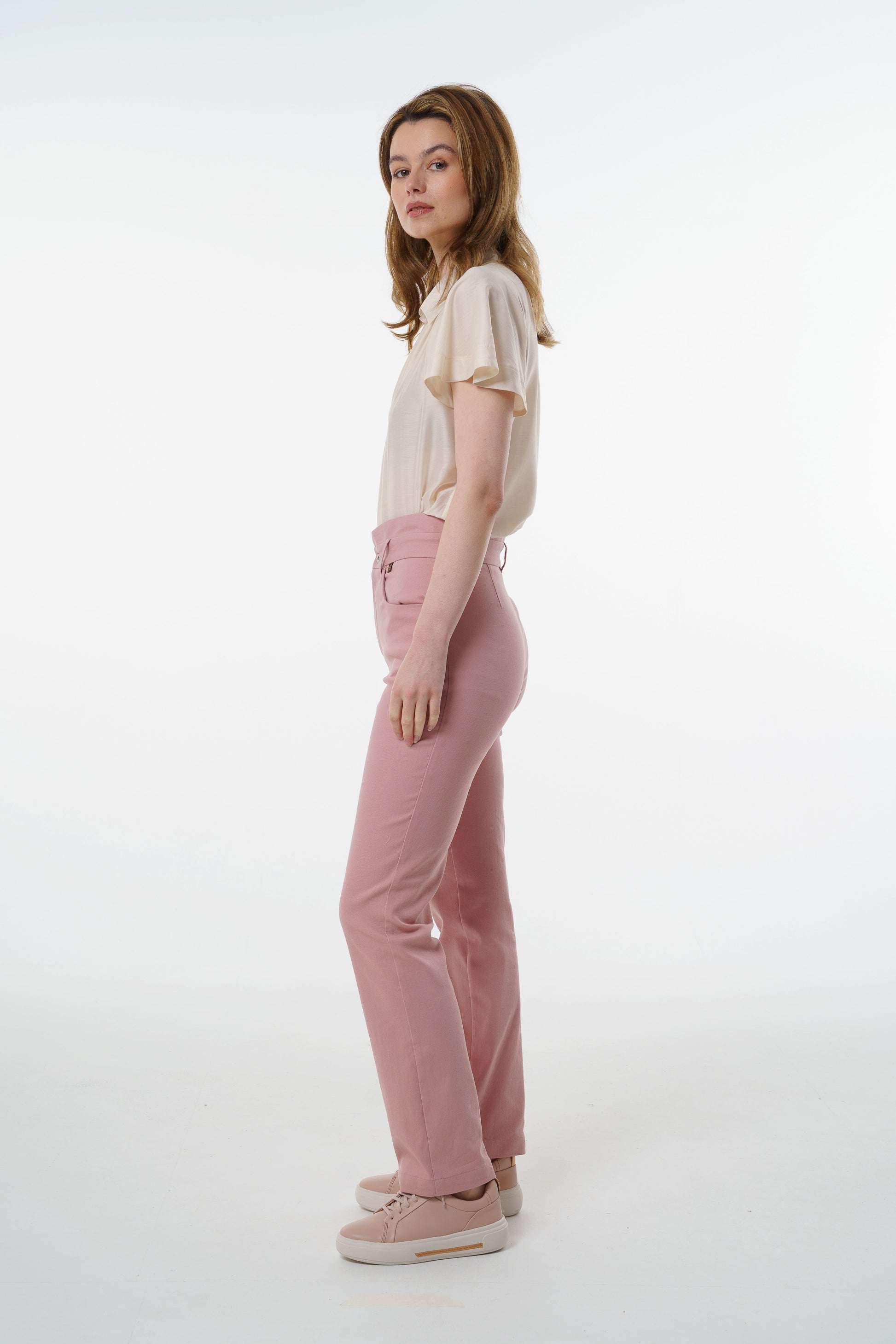 Rose‑dust high‑waisted stretch denim trousers with layered waistband and straight‑leg cut, worn by a model, profile studio view.