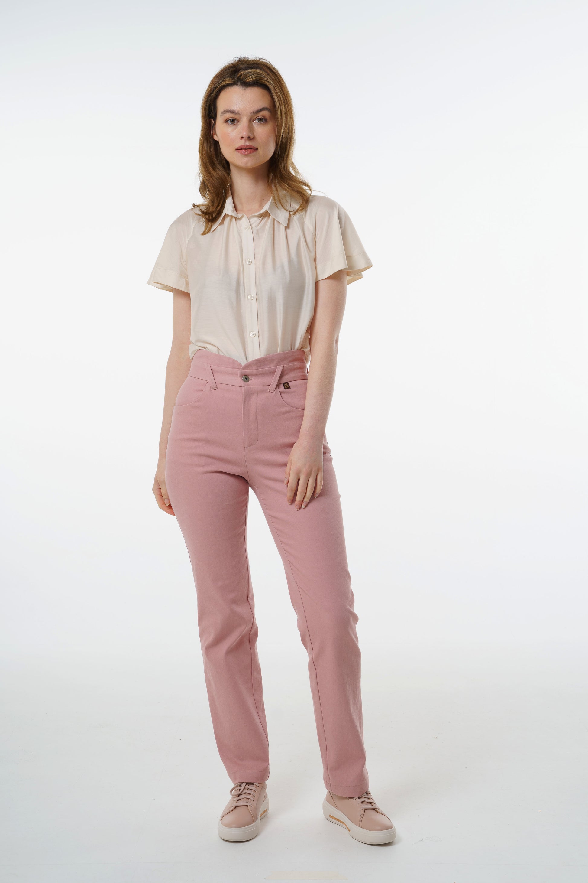 Rose‑dust high‑waisted stretch denim trousers with layered waistband and straight‑leg silhouette, worn by a model with a cream short‑sleeve blouse, front studio view.