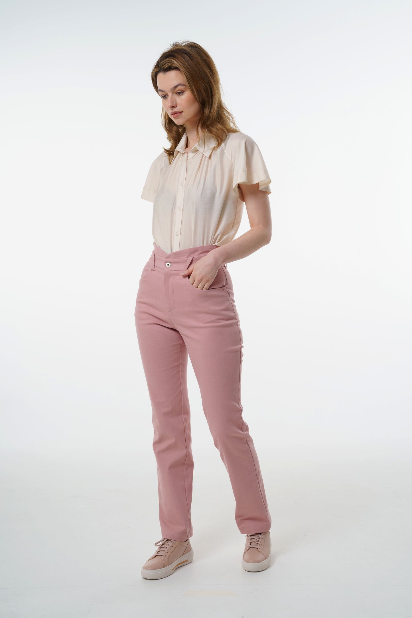 Rose‑dust high‑waisted stretch denim trousers with layered waistband, front pockets, and tailored fit, worn by a model, front studio shot.