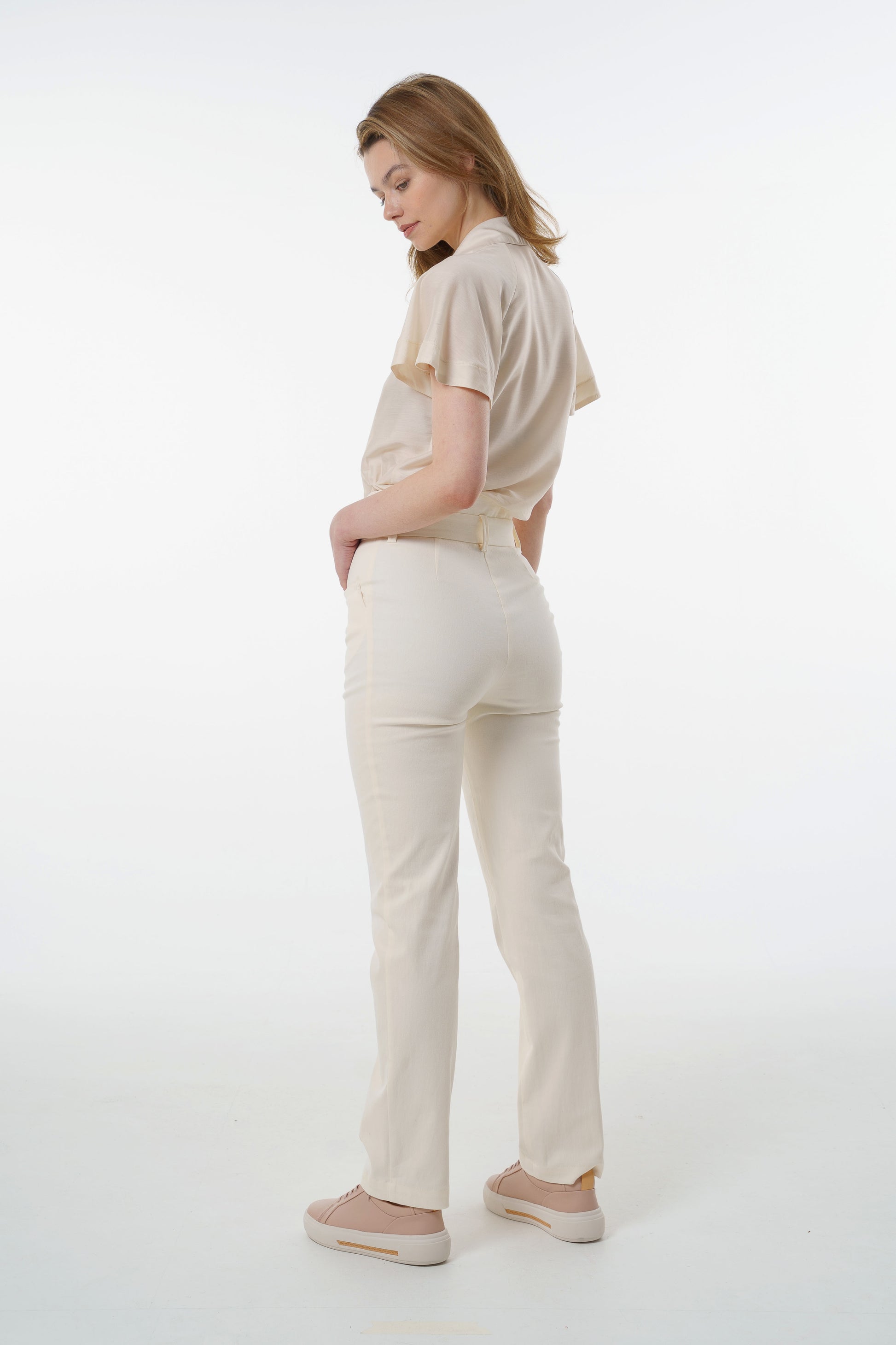 Cream high‑waisted stretch denim trousers with layered waistband and straight‑leg silhouette, worn by a model, angled back studio view.