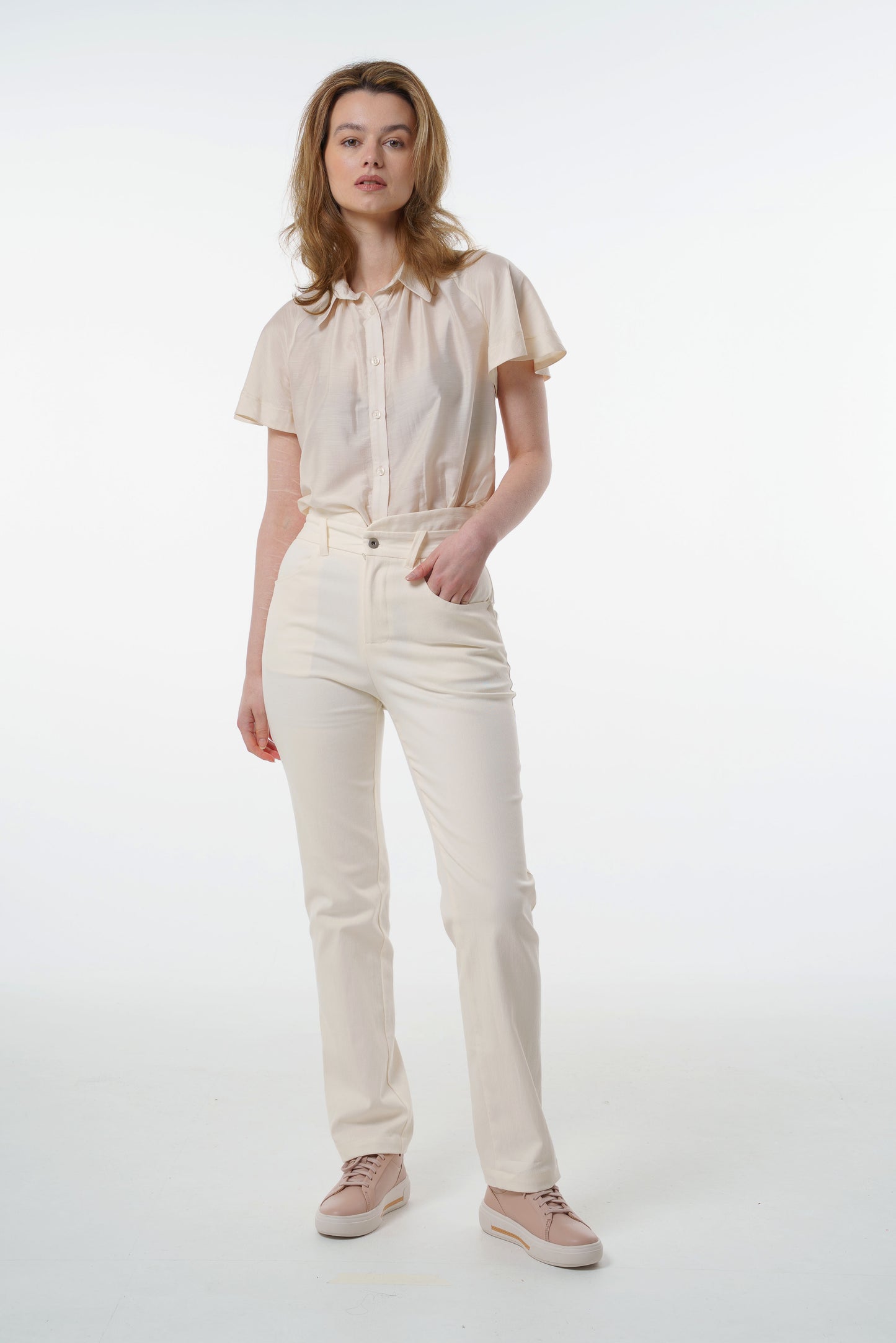 Cream high‑waisted stretch denim trousers with layered waistband and tailored straight‑leg fit, worn by a model with a beige short‑sleeve blouse, front studio view.