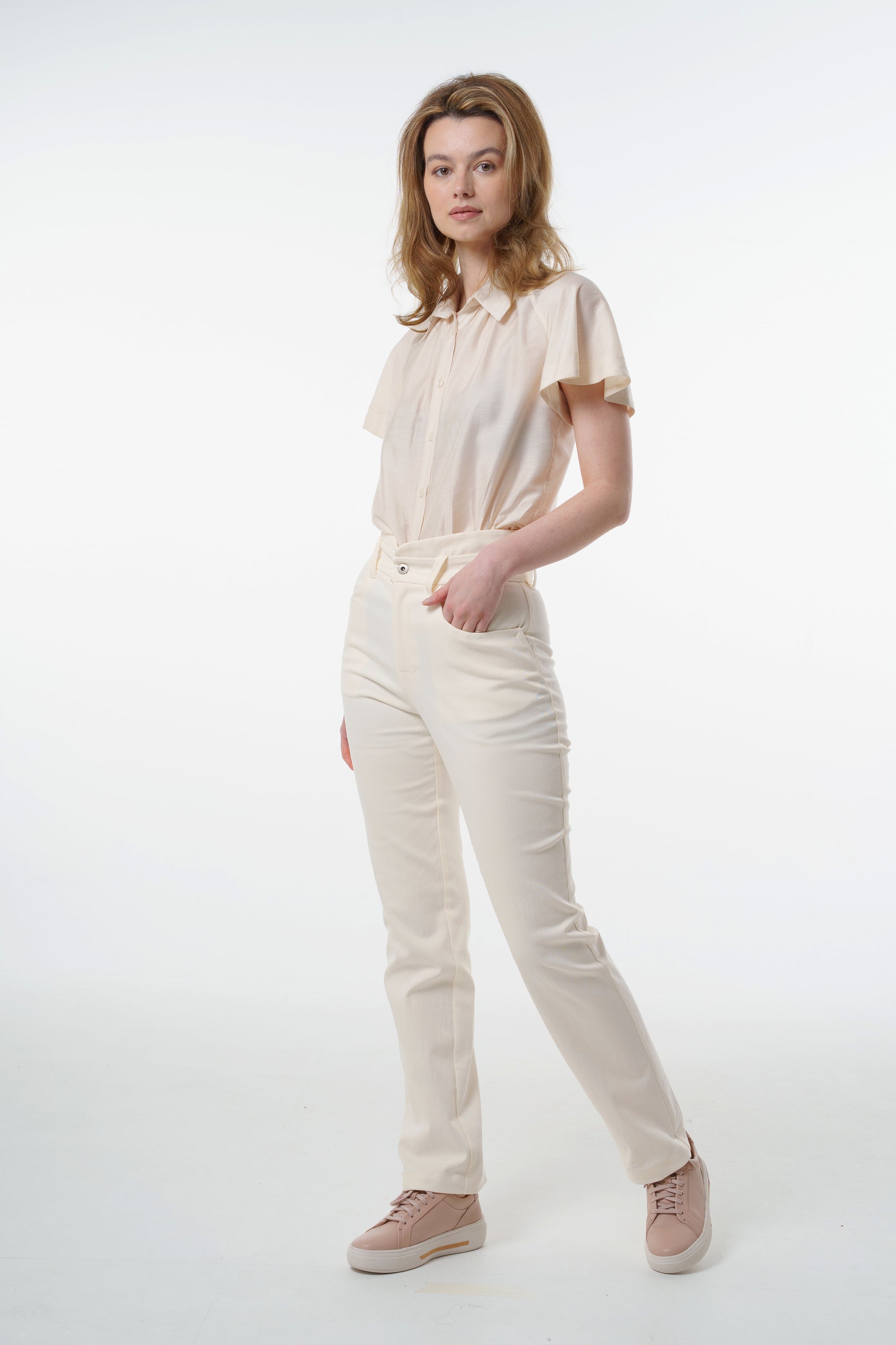 Cream high‑waisted stretch denim trousers with layered waistband, front pockets, and clean straight‑leg line, worn by a model, front studio shot.