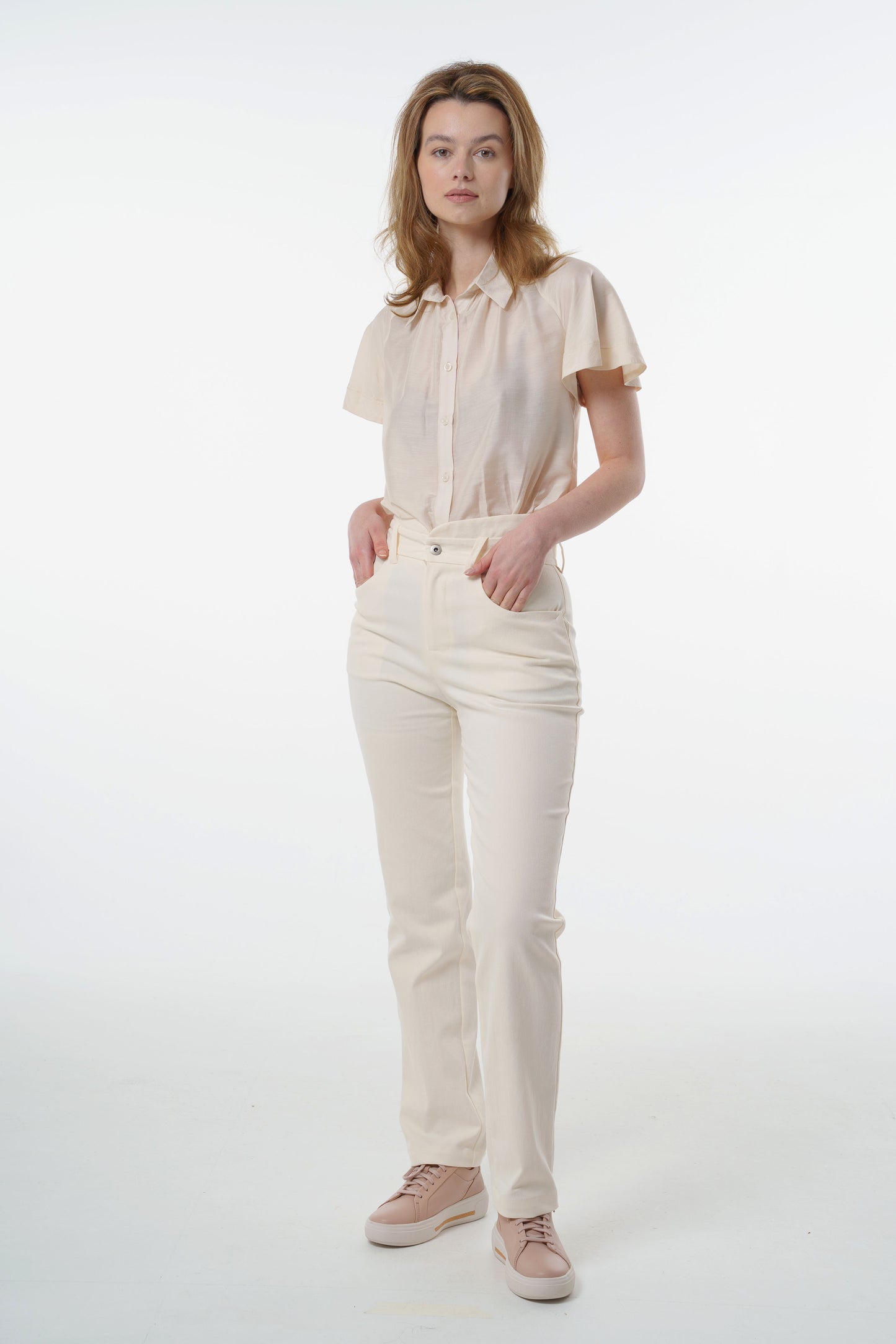 Cream high‑waisted stretch denim trousers in stretch denim with layered waistband and straight‑leg silhouette, worn by a model, full‑length front studio view.