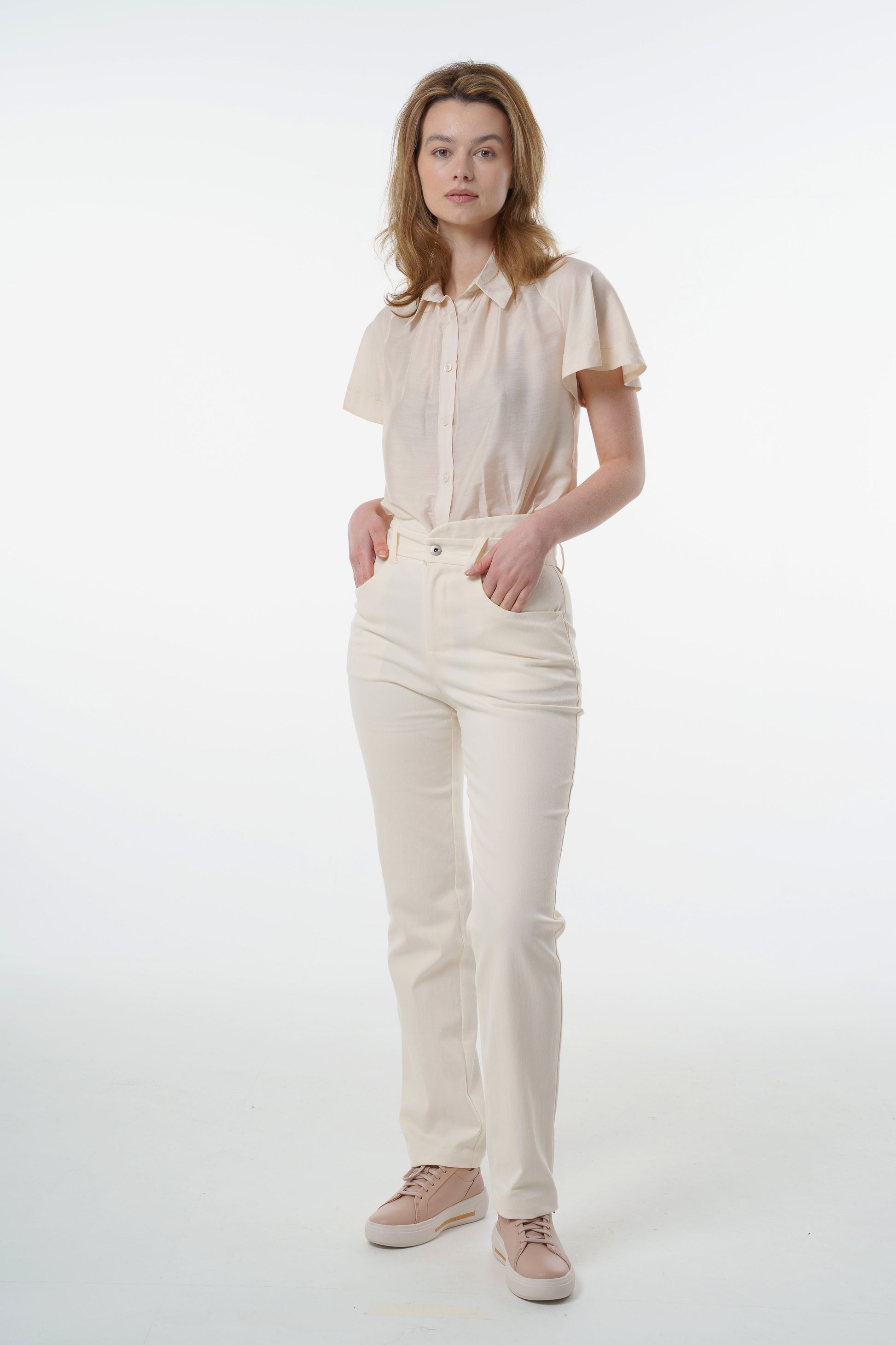Cream high‑waisted stretch denim trousers in stretch denim with layered waistband and straight‑leg silhouette, worn by a model, full‑length front studio view.