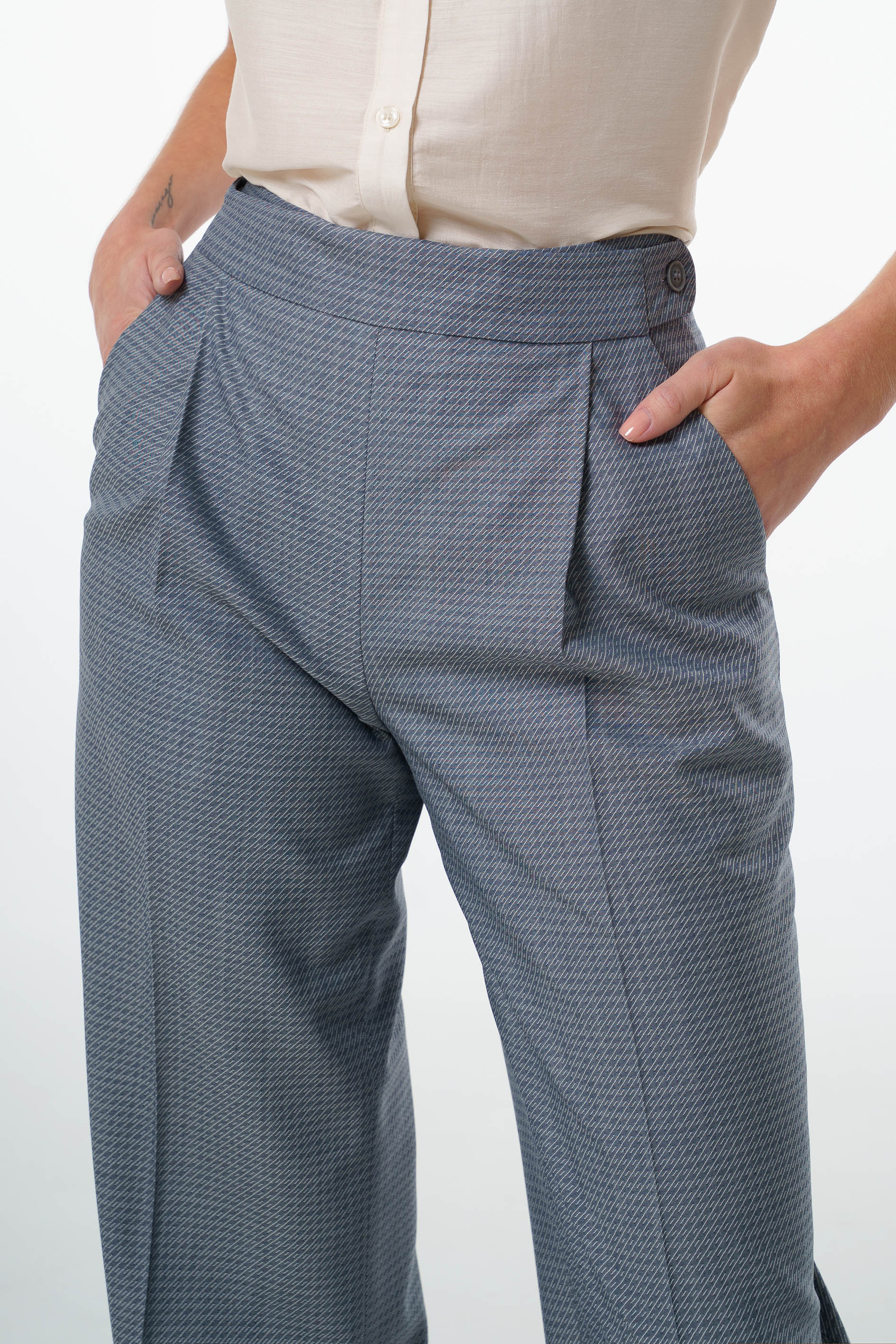 Mid‑waisted wide‑leg trousers in virgin wool featuring an adjustable side‑button waistband, front pleats, and tailored pocket construction, worn by a model, close‑up studio shot.