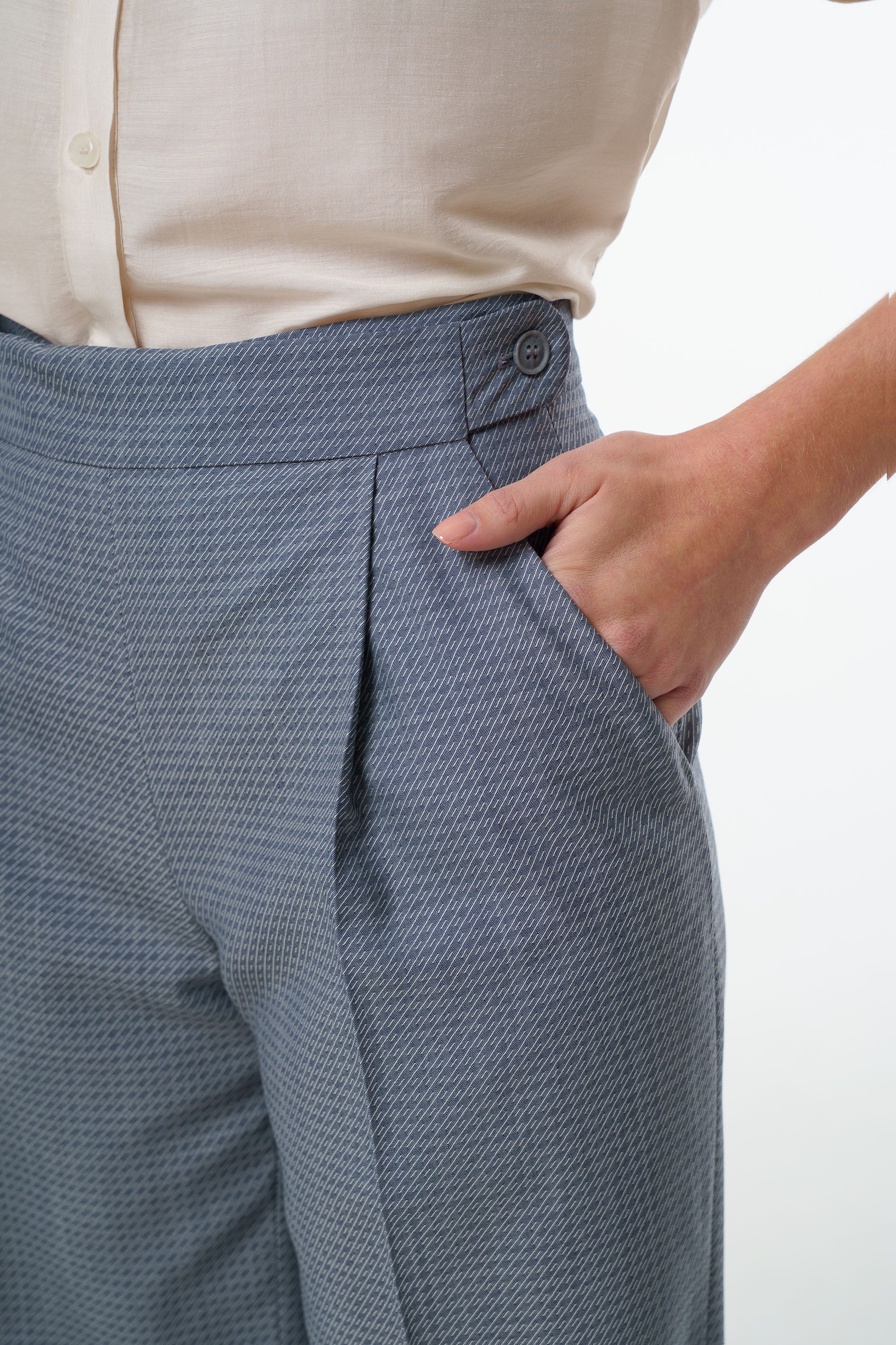 - Mid‑waisted wide‑leg virgin wool trousers with an adjustable side‑button waistband and diagonal patterned weave, worn by a model, close‑up studio view.