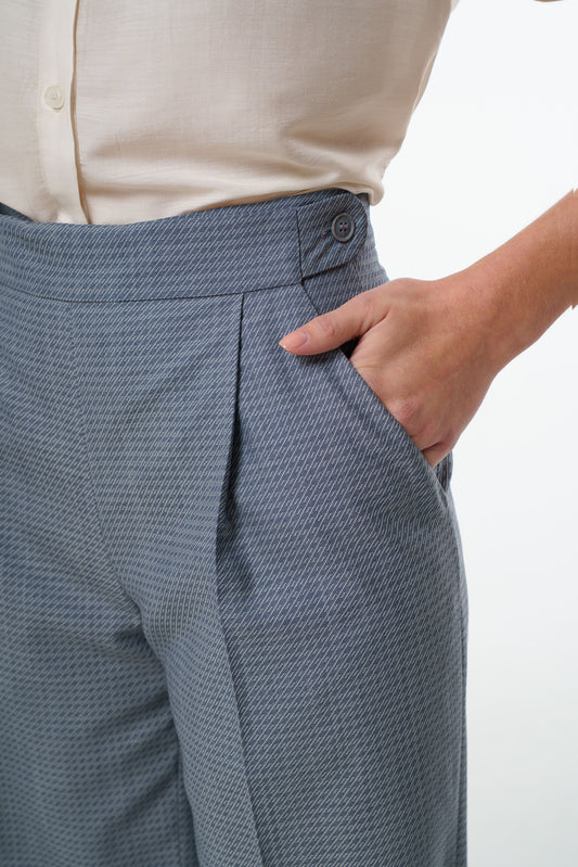 - Mid‑waisted wide‑leg virgin wool trousers with an adjustable side‑button waistband and diagonal patterned weave, worn by a model, close‑up studio view.