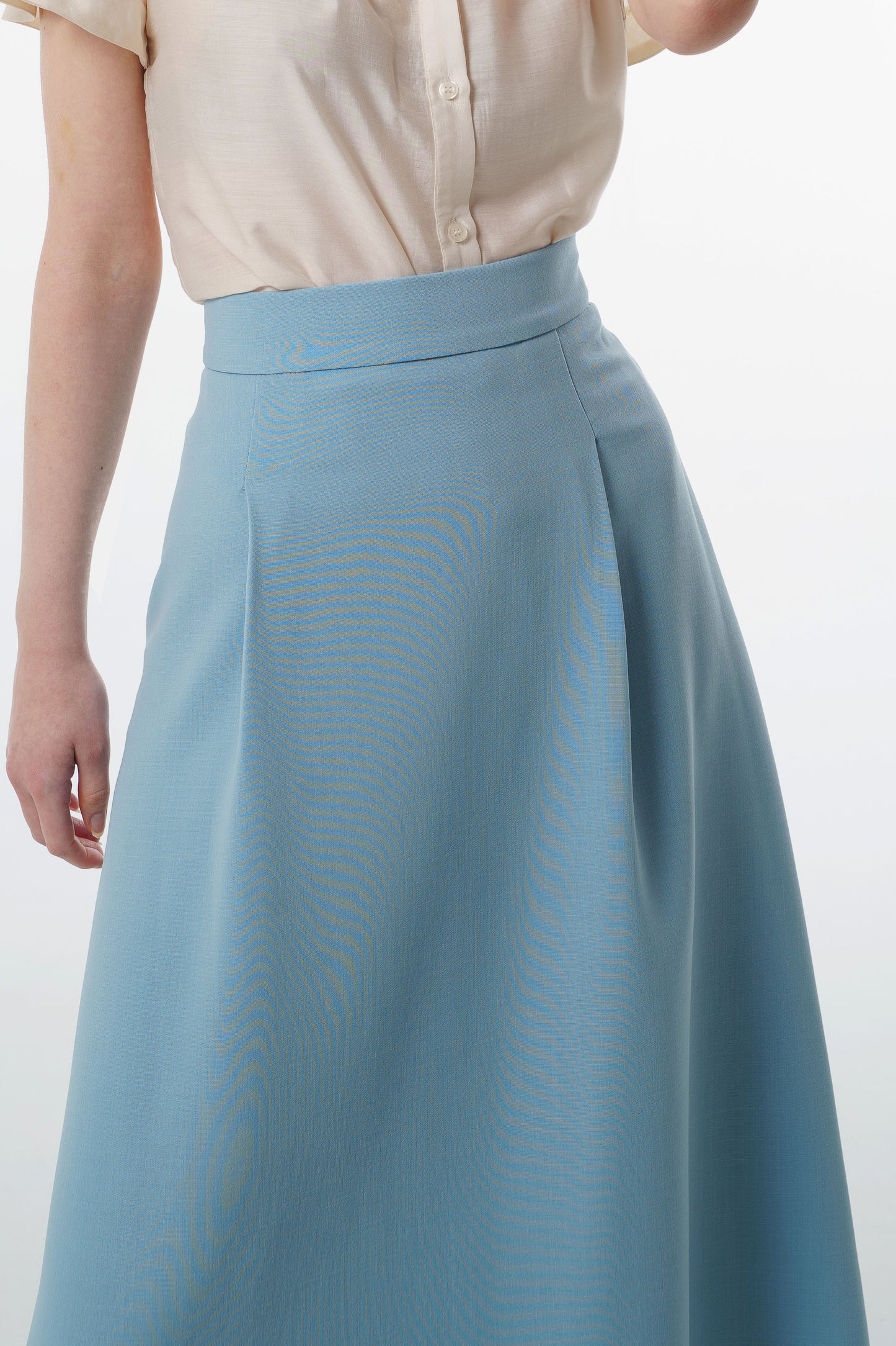 Close‑up of light blue virgin‑wool A‑line midi skirt showing high‑waisted construction and subtle pleating.