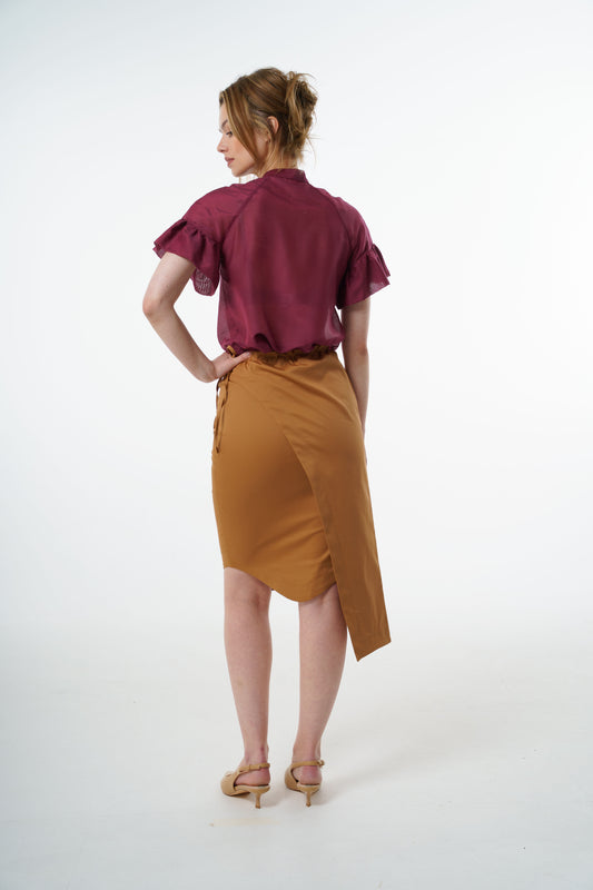 Camel cotton–viscose wrap pencil skirt with asymmetric overlay and side tie, worn by a model, back studio view.
