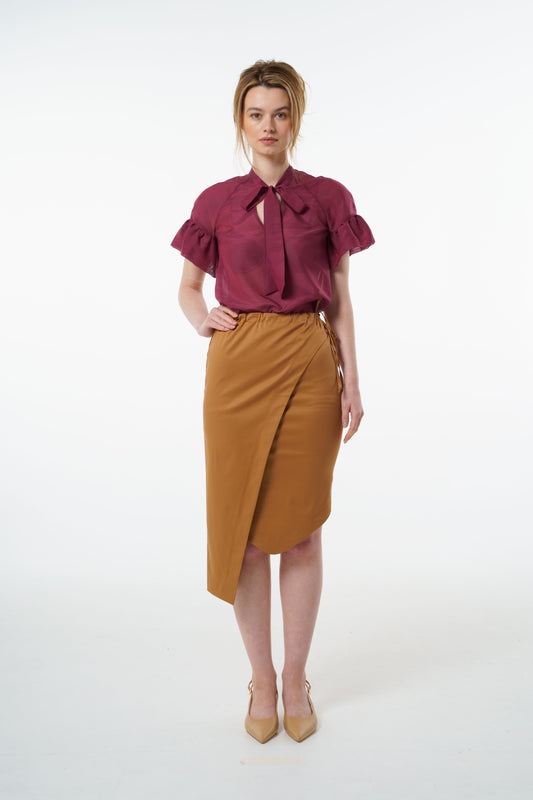 Camel cotton–viscose wrap pencil skirt with asymmetric hem and side tie, worn by a model with a burgundy blouse, front studio view.