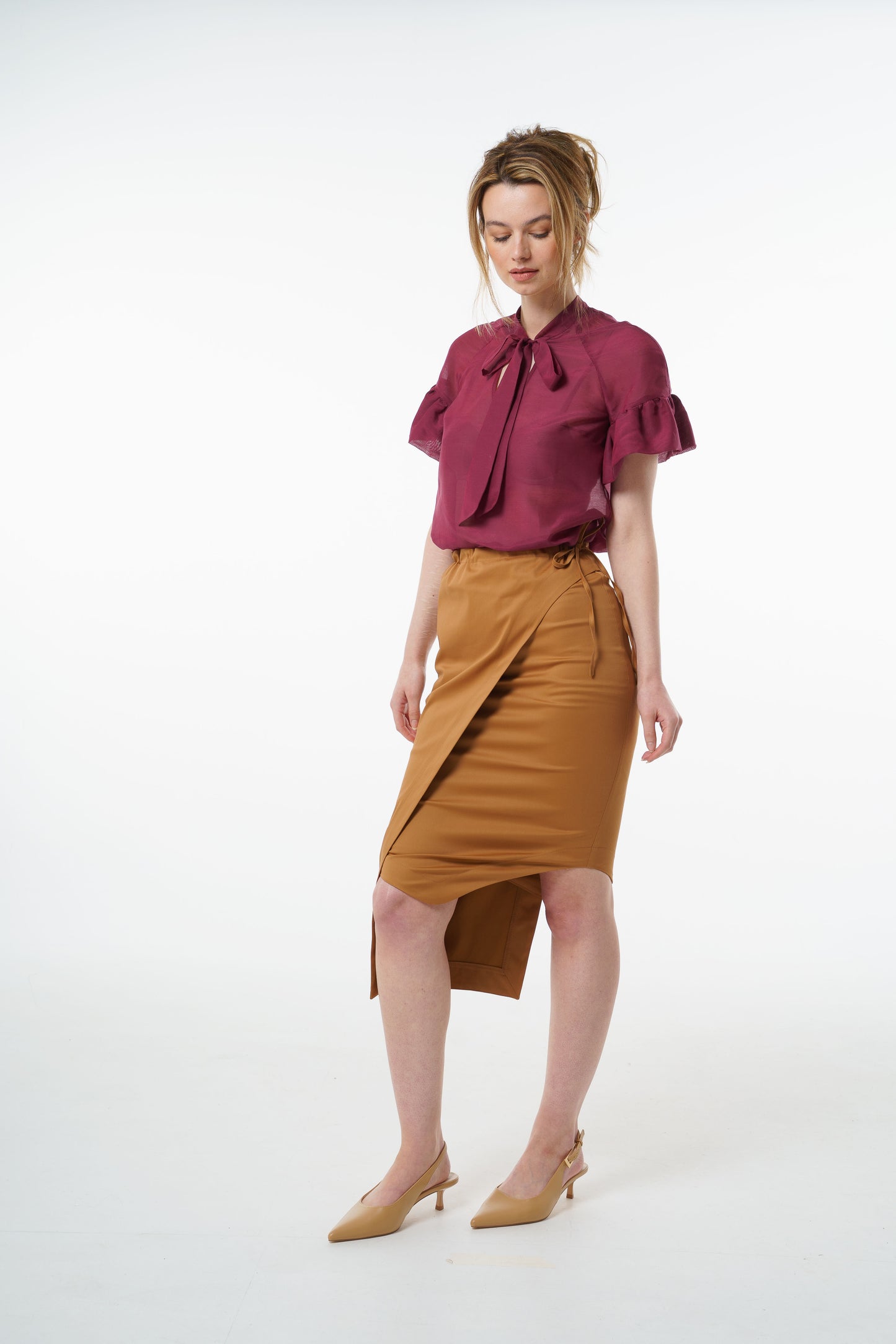 Camel cotton–viscose wrap pencil skirt with asymmetric hem and tied waist, worn by a model, front studio shot.