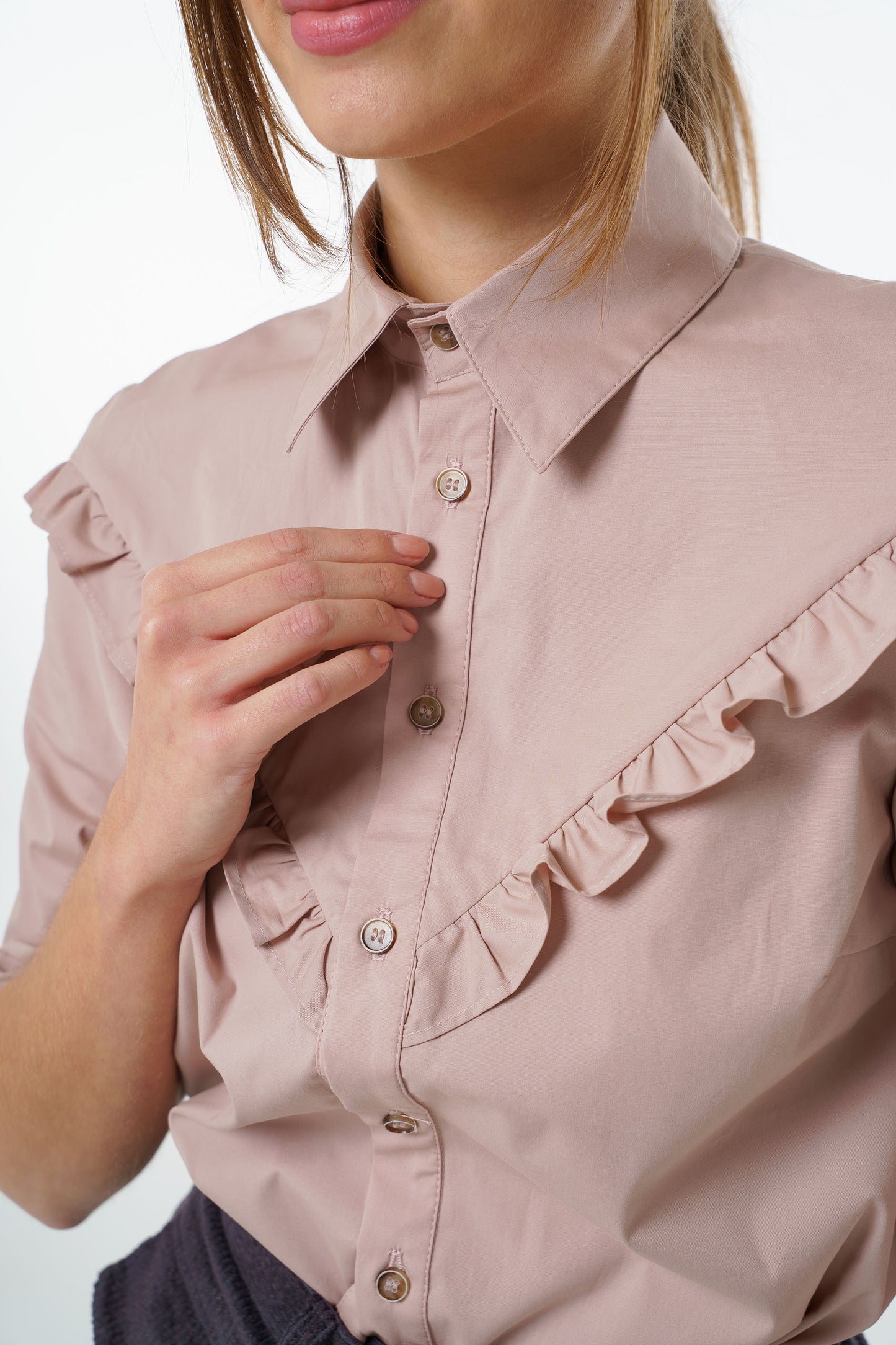 Blush cotton‑stretch shirt with V‑front ruffle, classic collar, and button‑front placket, worn by a model, close‑up studio view.