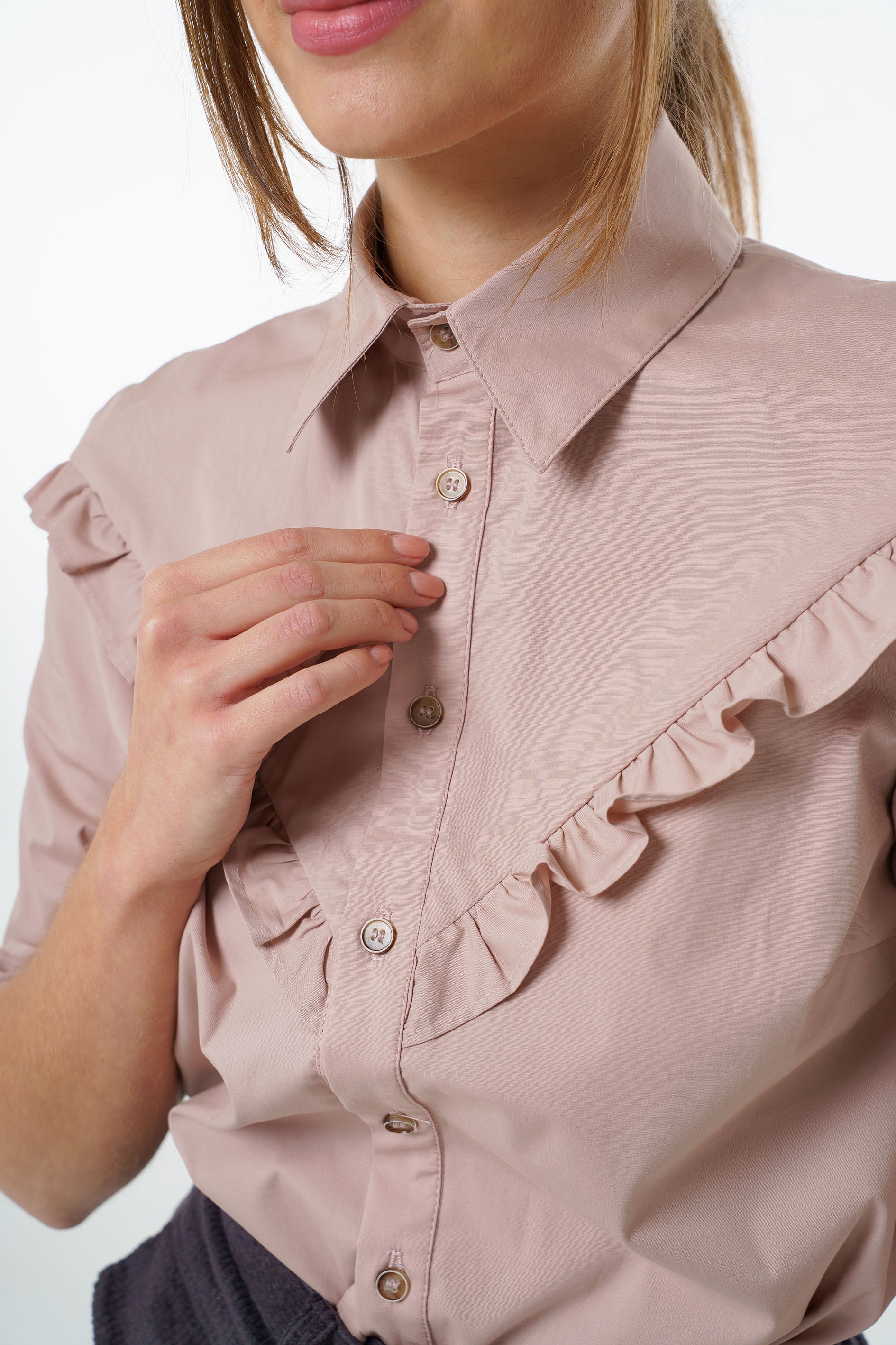 Blush cotton‑stretch shirt with V‑front ruffle, classic collar, and button‑front placket, worn by a model, close‑up studio view.