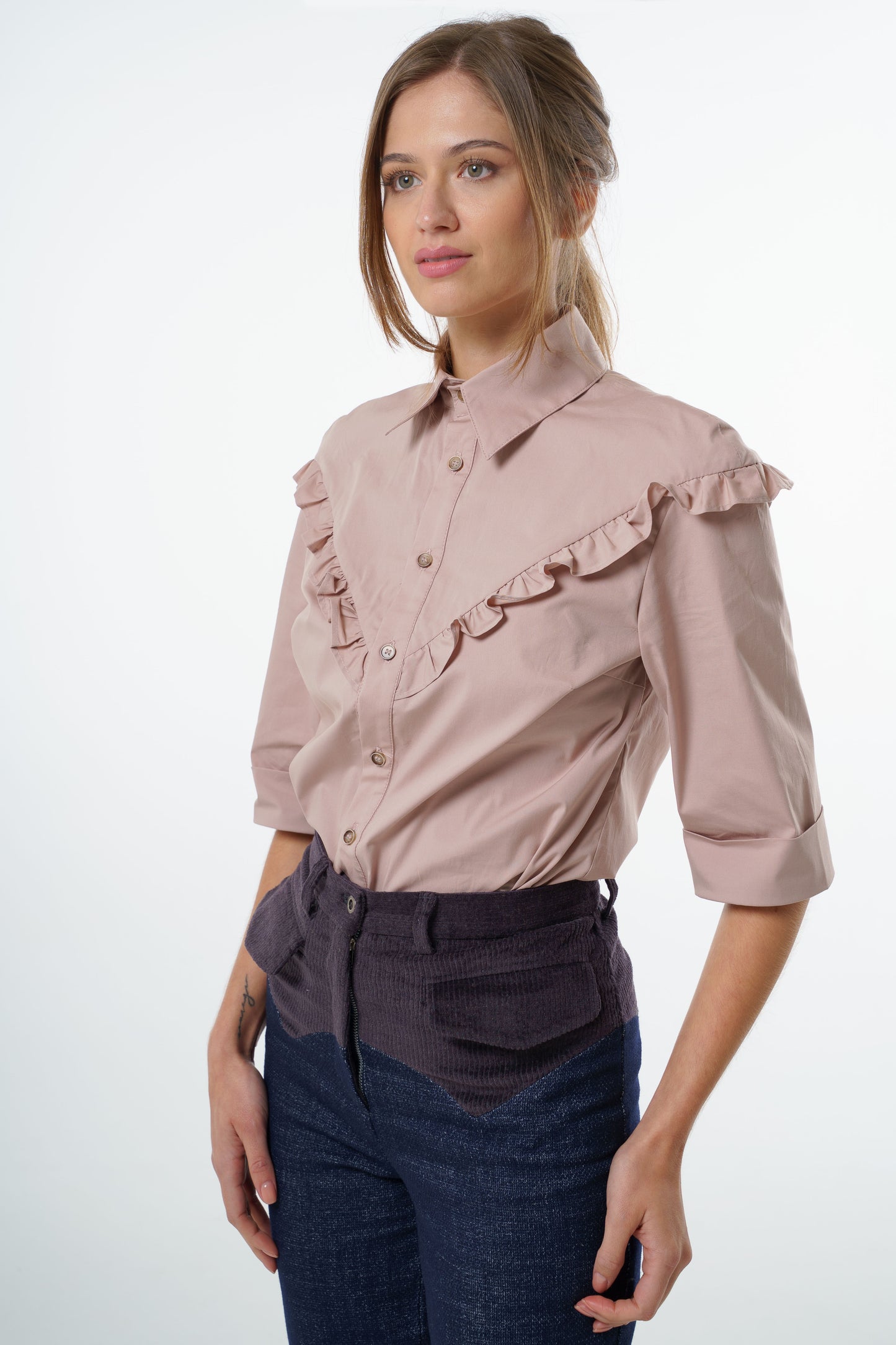 Blush cotton‑stretch shirt with V‑front ruffle, structured collar, and three‑quarter sleeves, worn by a model with high‑waisted two‑tone trousers, front studio view.