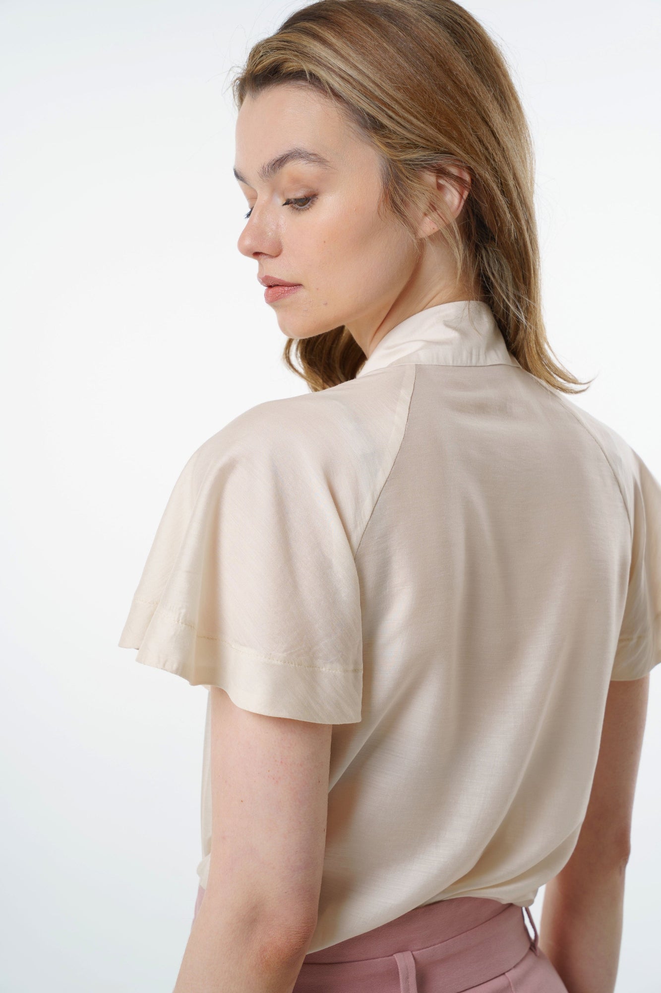 - Ivory short‑sleeve silk–viscose blouse with flared raglan sleeves and fluid back silhouette, worn by a model with high‑waisted rose‑dust trousers, angled back studio view.