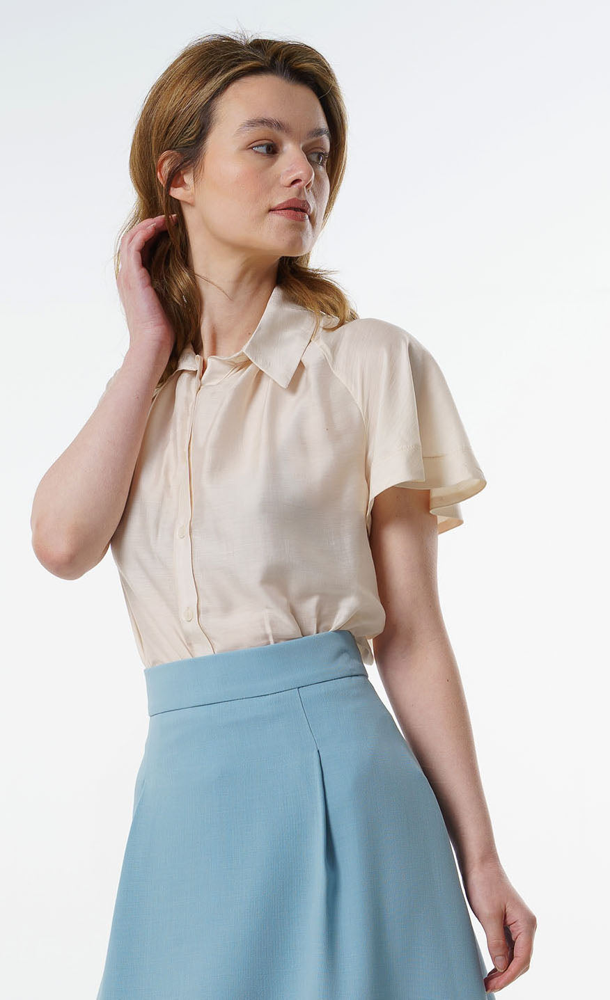 Ivory short‑sleeve silk–viscose blouse with flared raglan sleeves and soft drape, worn by a model with a high‑waisted blue skirt, angled studio view.